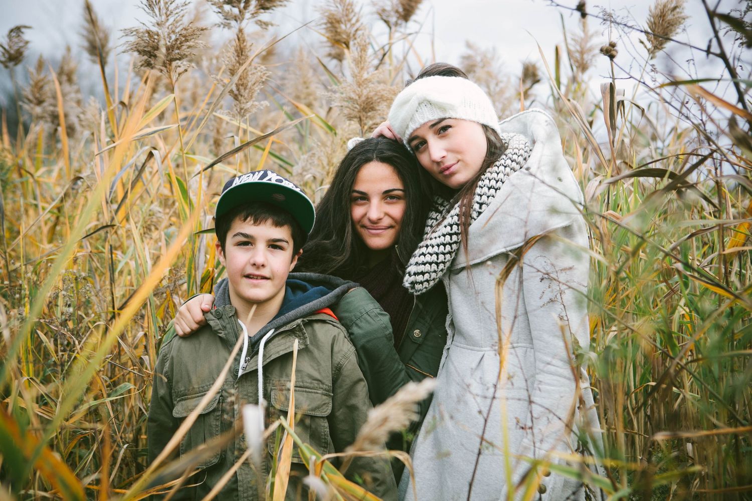 Three figures pose together amid tall golden pampas grass during an outdoor photo session.