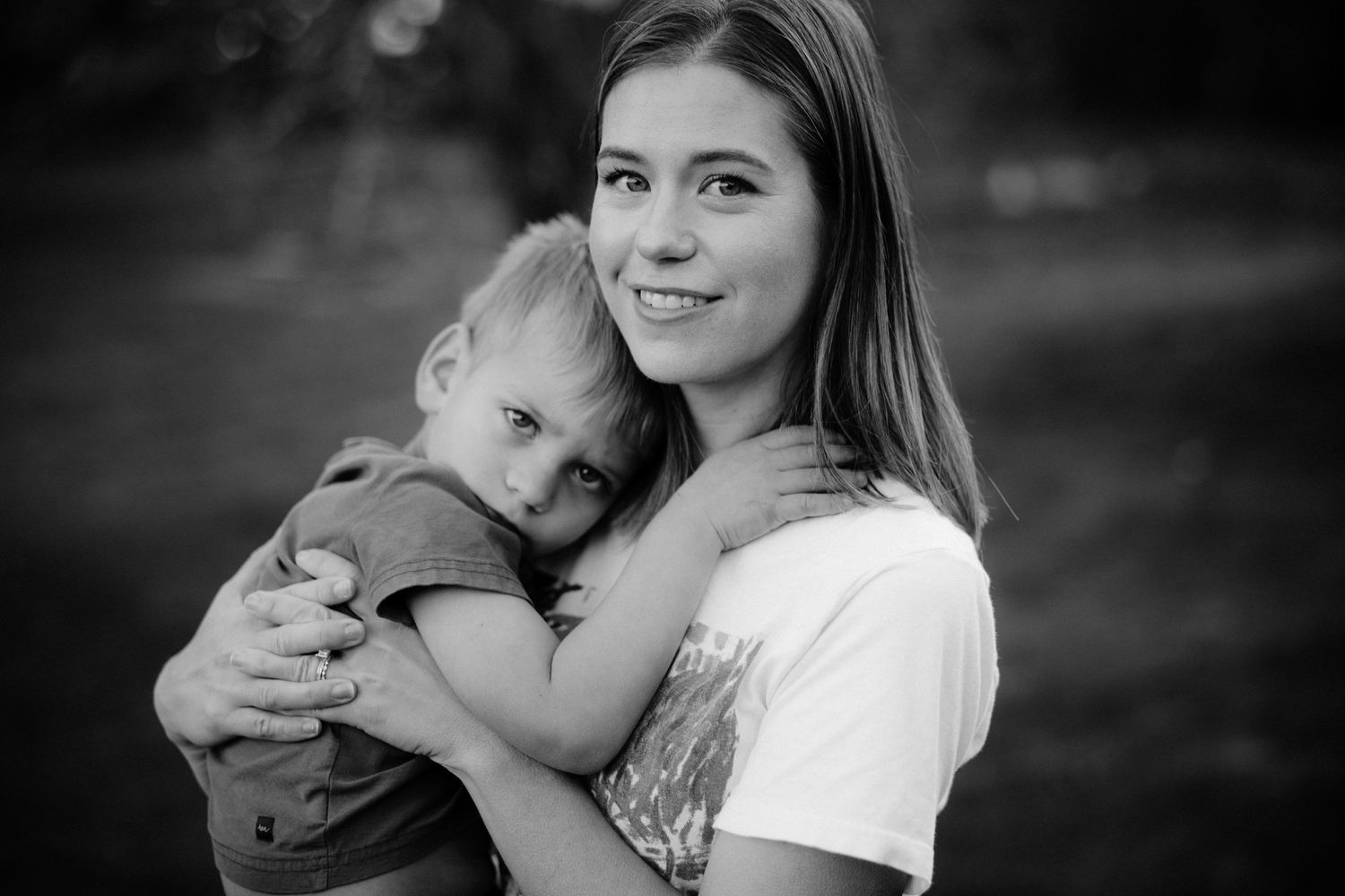 Black and white portrait of mother and child embracing outdoors with soft bokeh background.