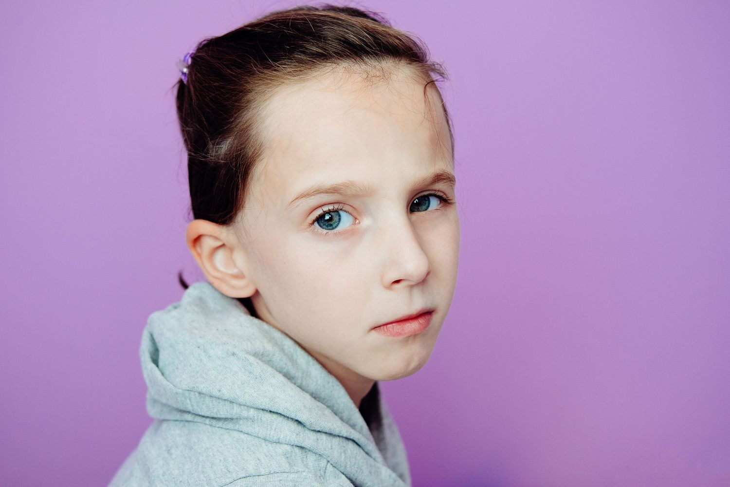 Portrait of young person in gray hoodie against purple background.