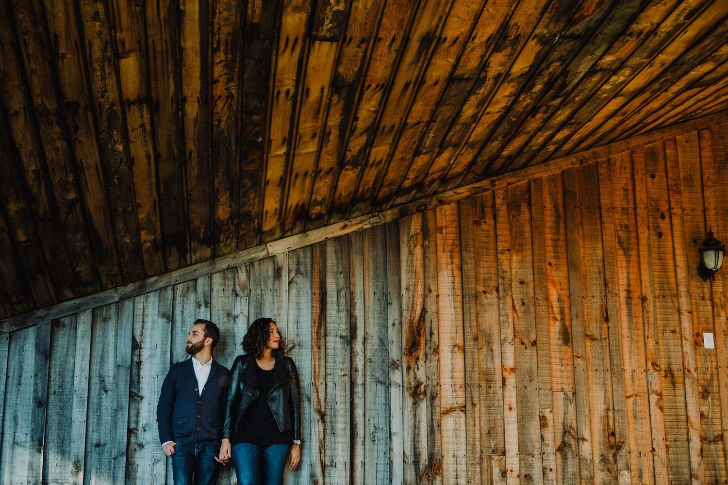 Couple standing against rustic wooden barn wall during moody photoshoot.