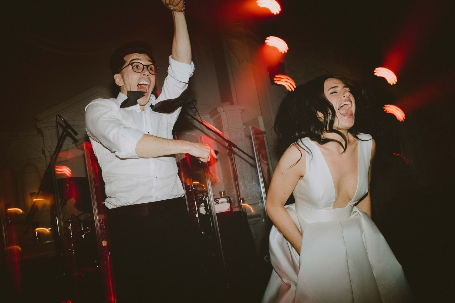A couple dances joyfully under dramatic red lighting at their wedding reception.
