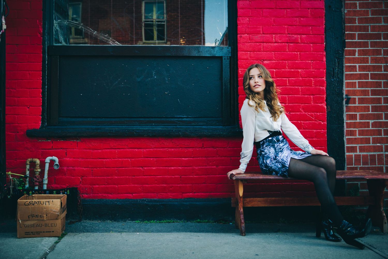 Lifestyle portrait of someone sitting on a bench against a red brick wall in an urban setting.