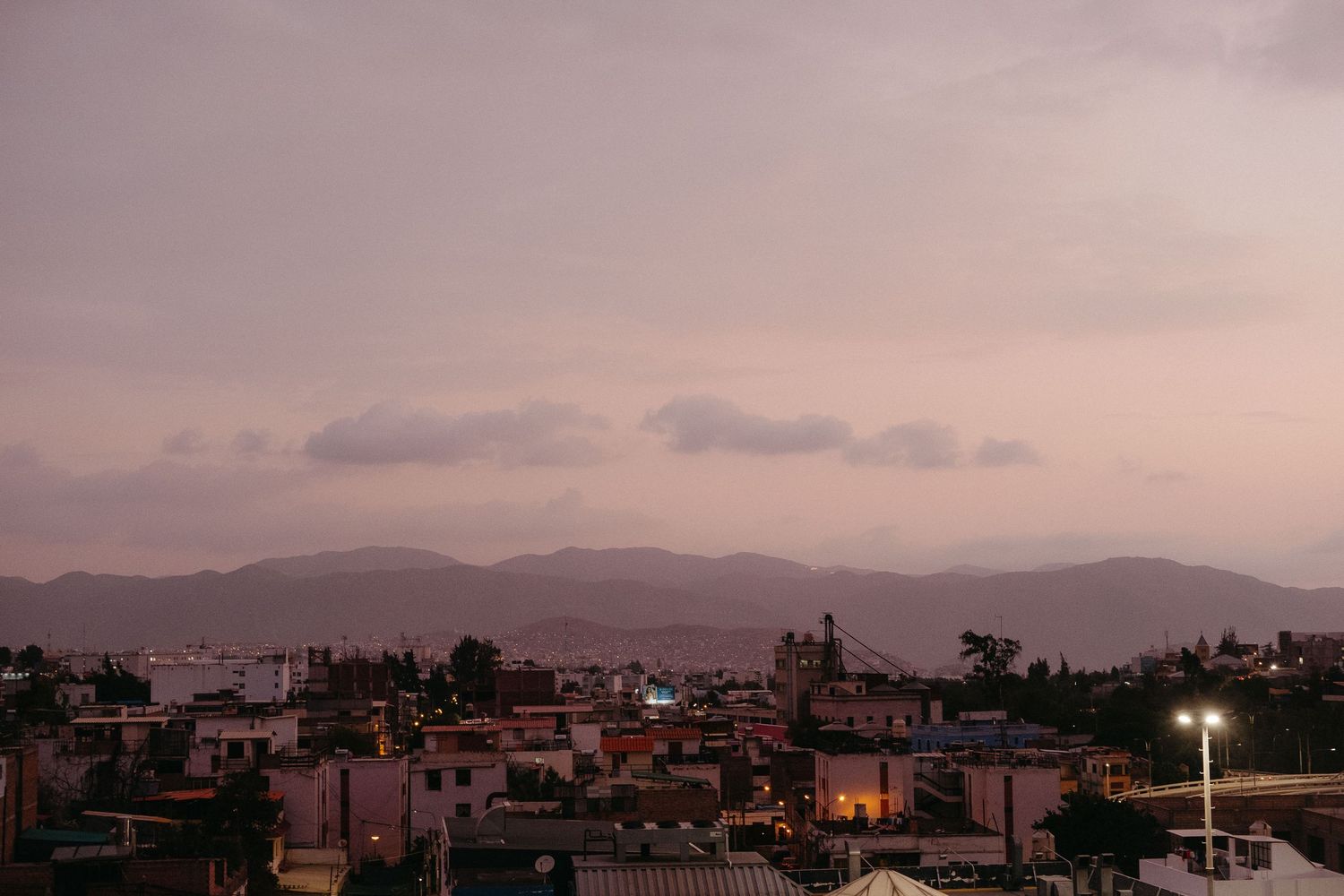 Sunset cityscape with mountains in the background and pink clouds.