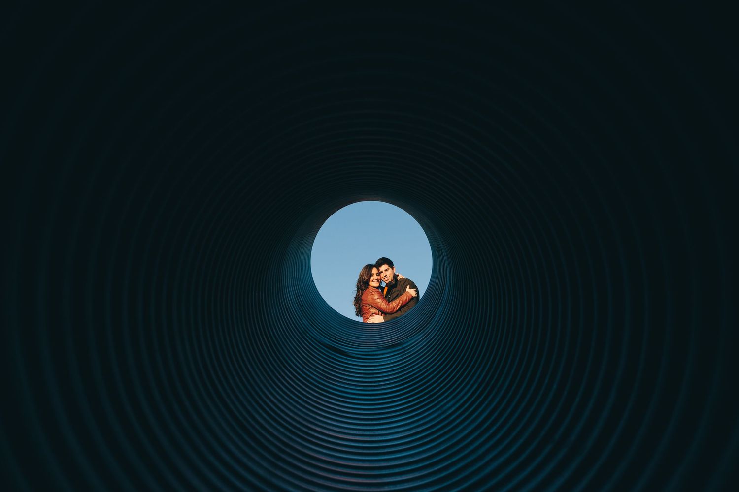 Silhouetted couple framed within circular tunnel with blue sky background.