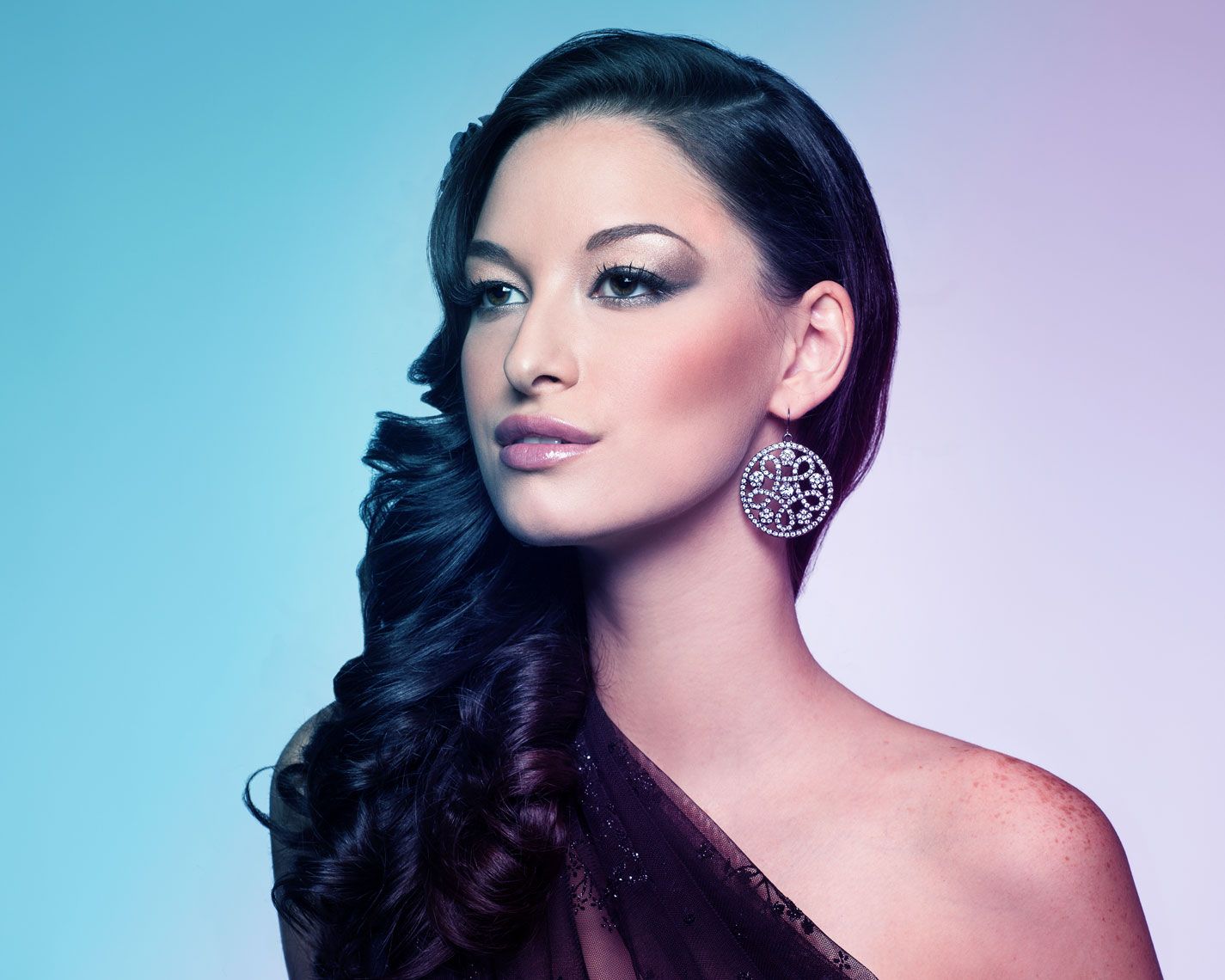 Glamour fashion portrait with dramatic lighting against blue and purple gradient background.
