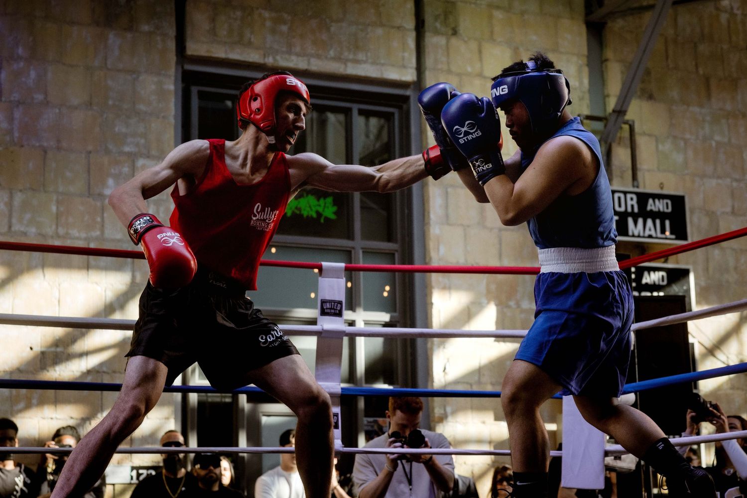 Boxers sparring in a ring wearing protective headgear and gloves.