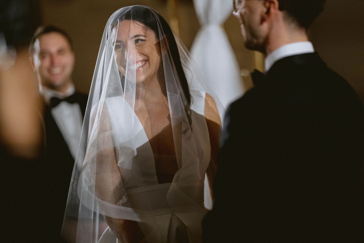 A radiant person in a wedding veil smiles brightly during an emotional ceremony moment.