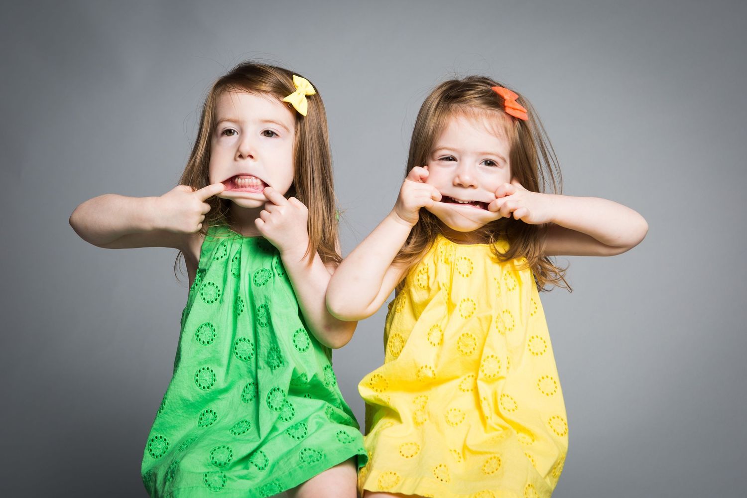 Two young children in bright green and yellow dresses making silly faces at the camera.