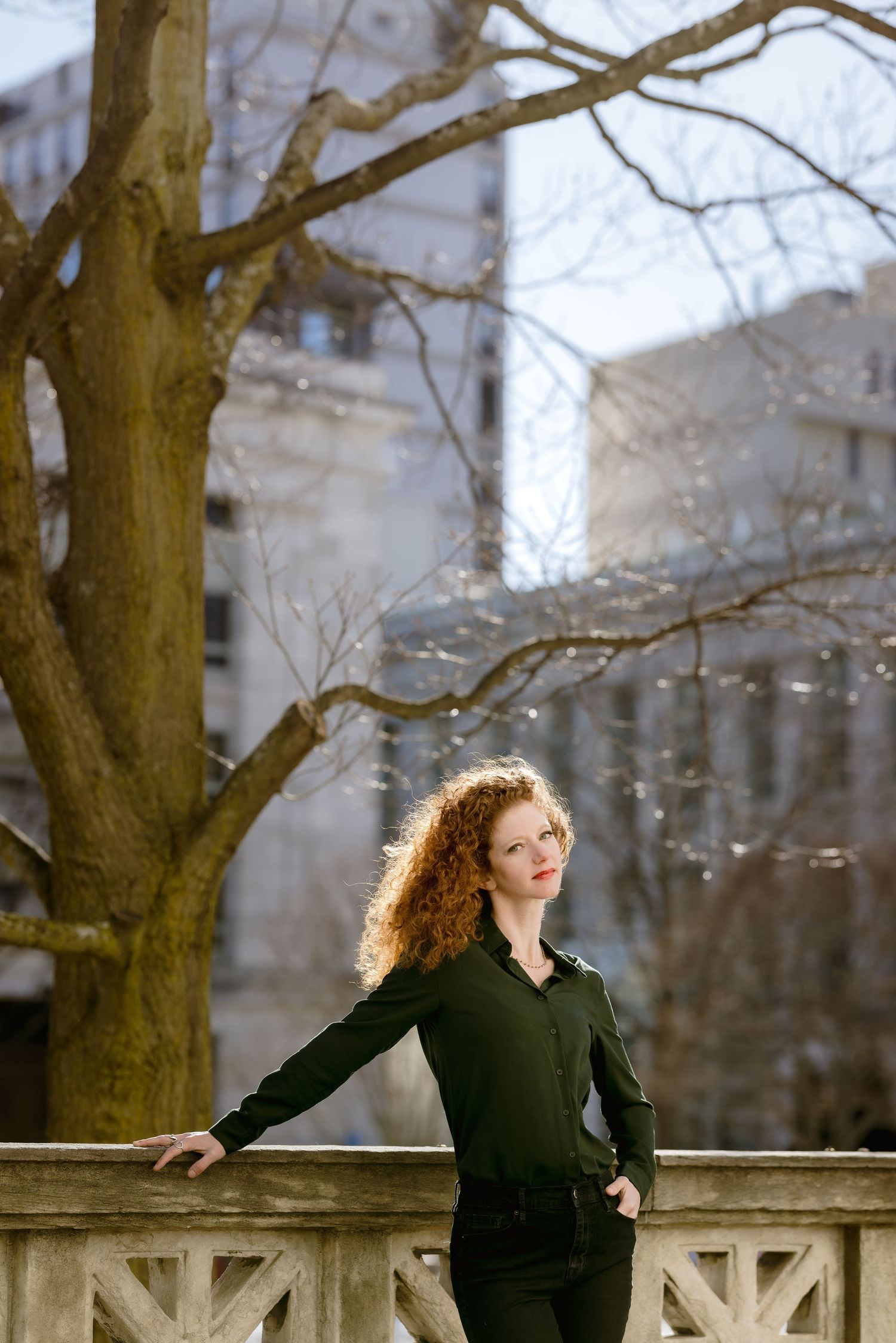 Person basking in sunlight on stone balustrade with bare tree branches.