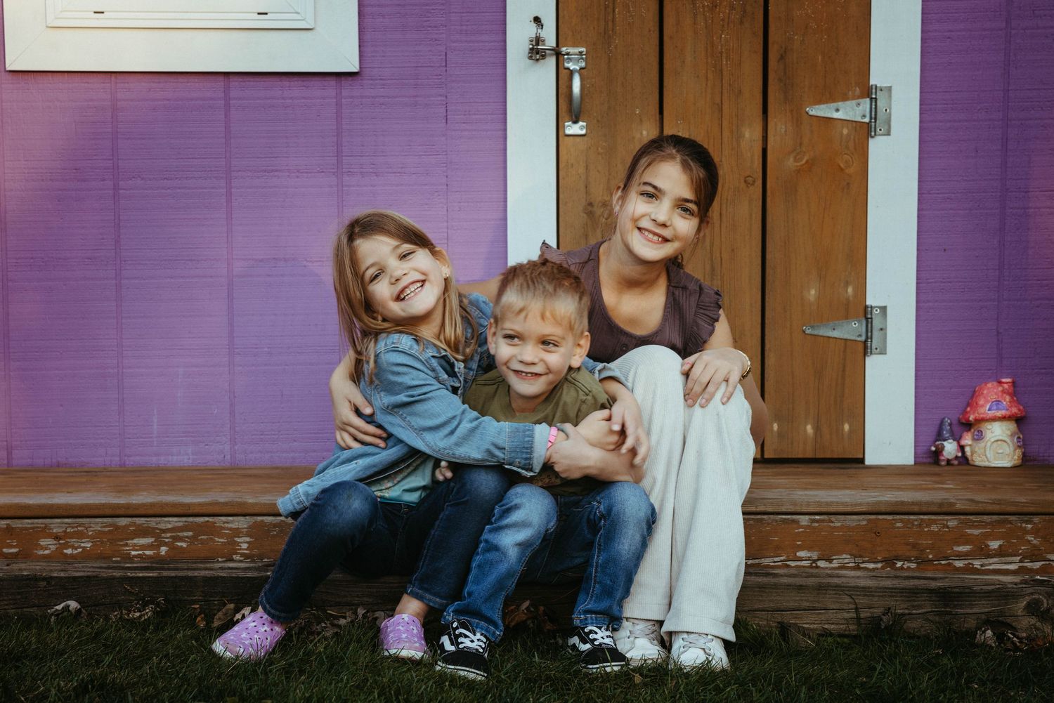 Group sitting together on purple-painted porch steps sharing a warm embrace.