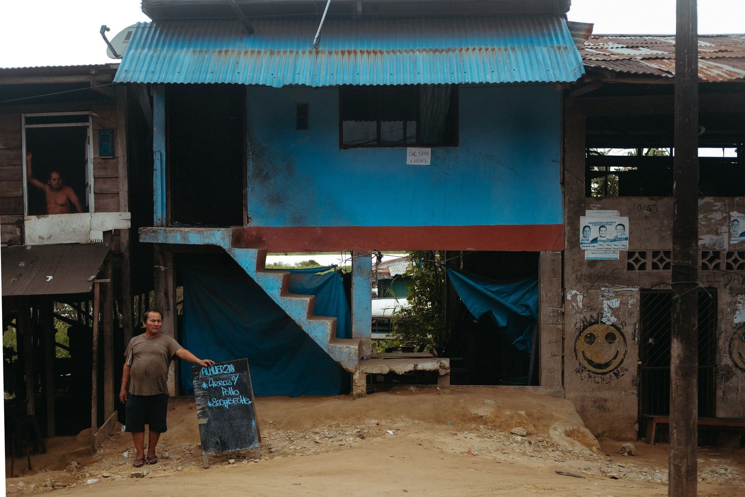 Row of small shops with blue awnings and simple architecture in tropical setting.