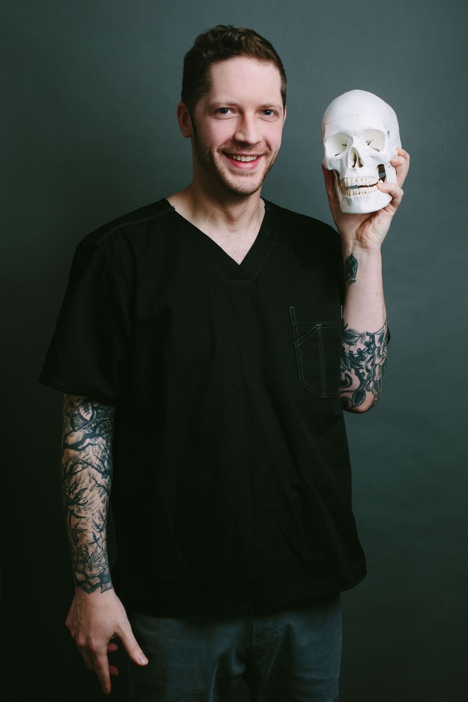 Person in black shirt with tattoo sleeve holding decorative skull against dark background.