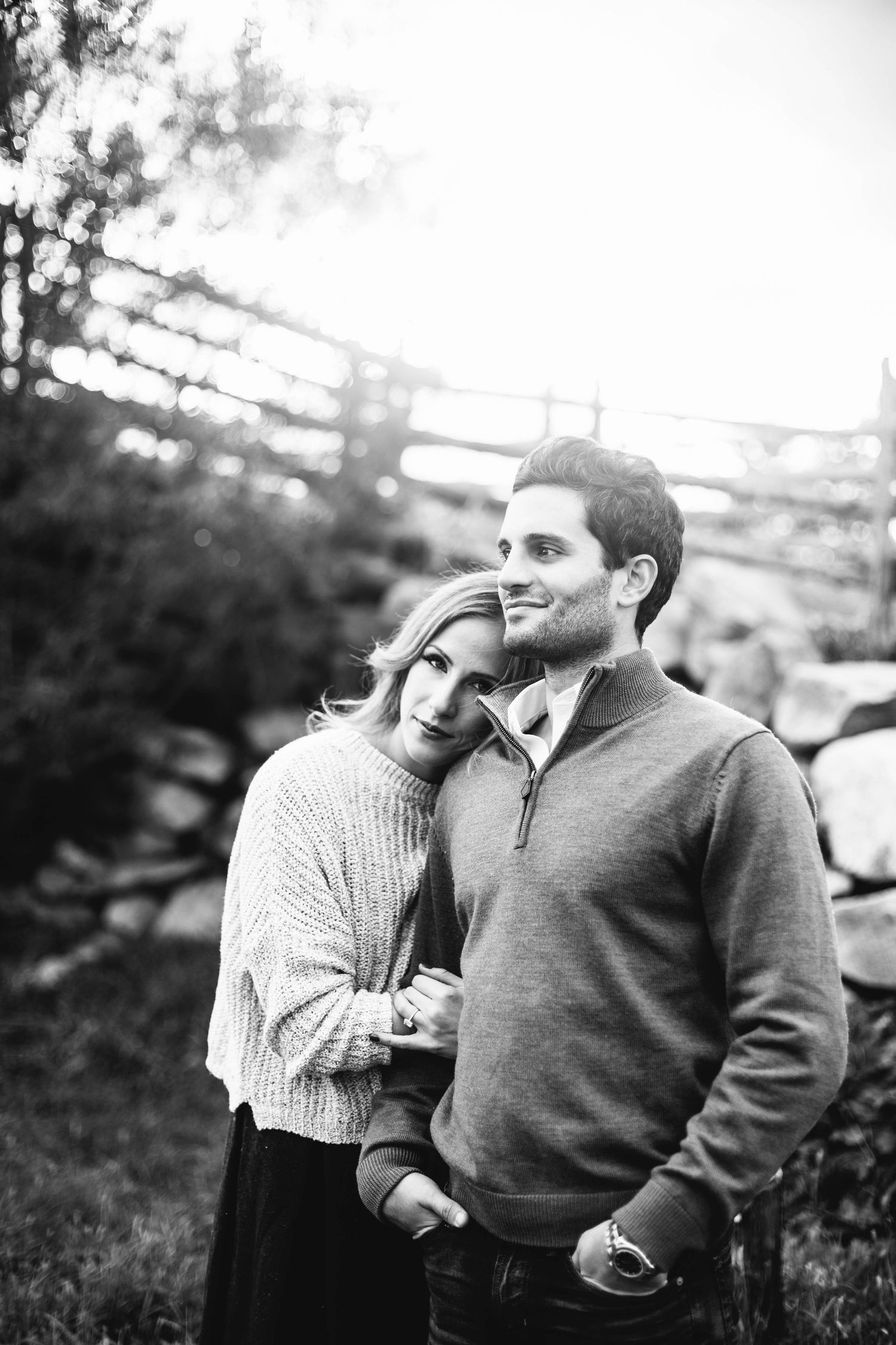 Romantic couple embracing outdoors in black and white photo with rustic fence backdrop.