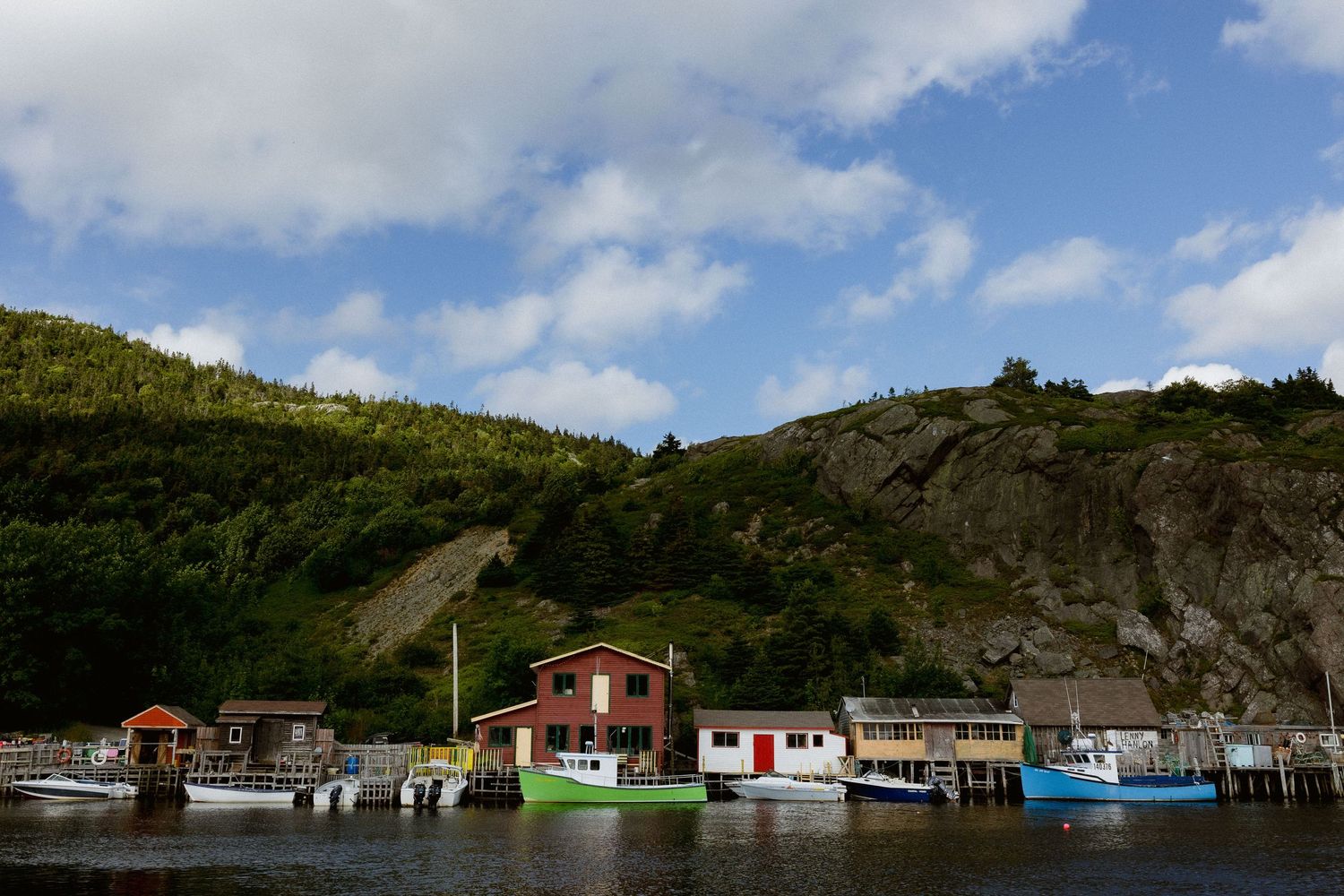 Colorful fishing houses on stilts along a coastal cliff under blue skies.