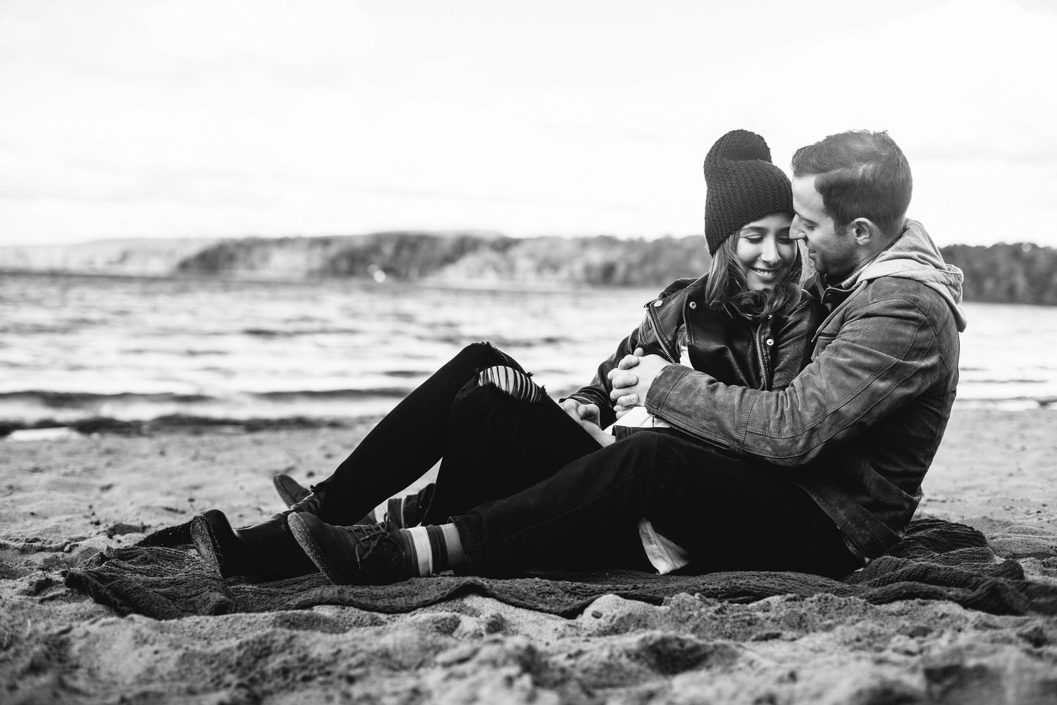 Couple sitting close together on beach blanket in black and white photograph.