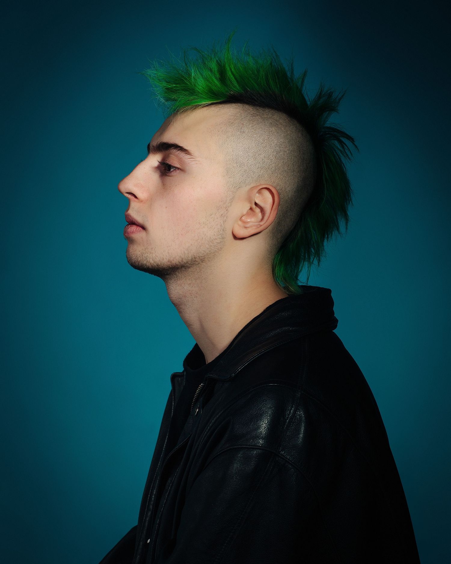 Profile portraits of person with green mohawk hairstyle against dark blue background.