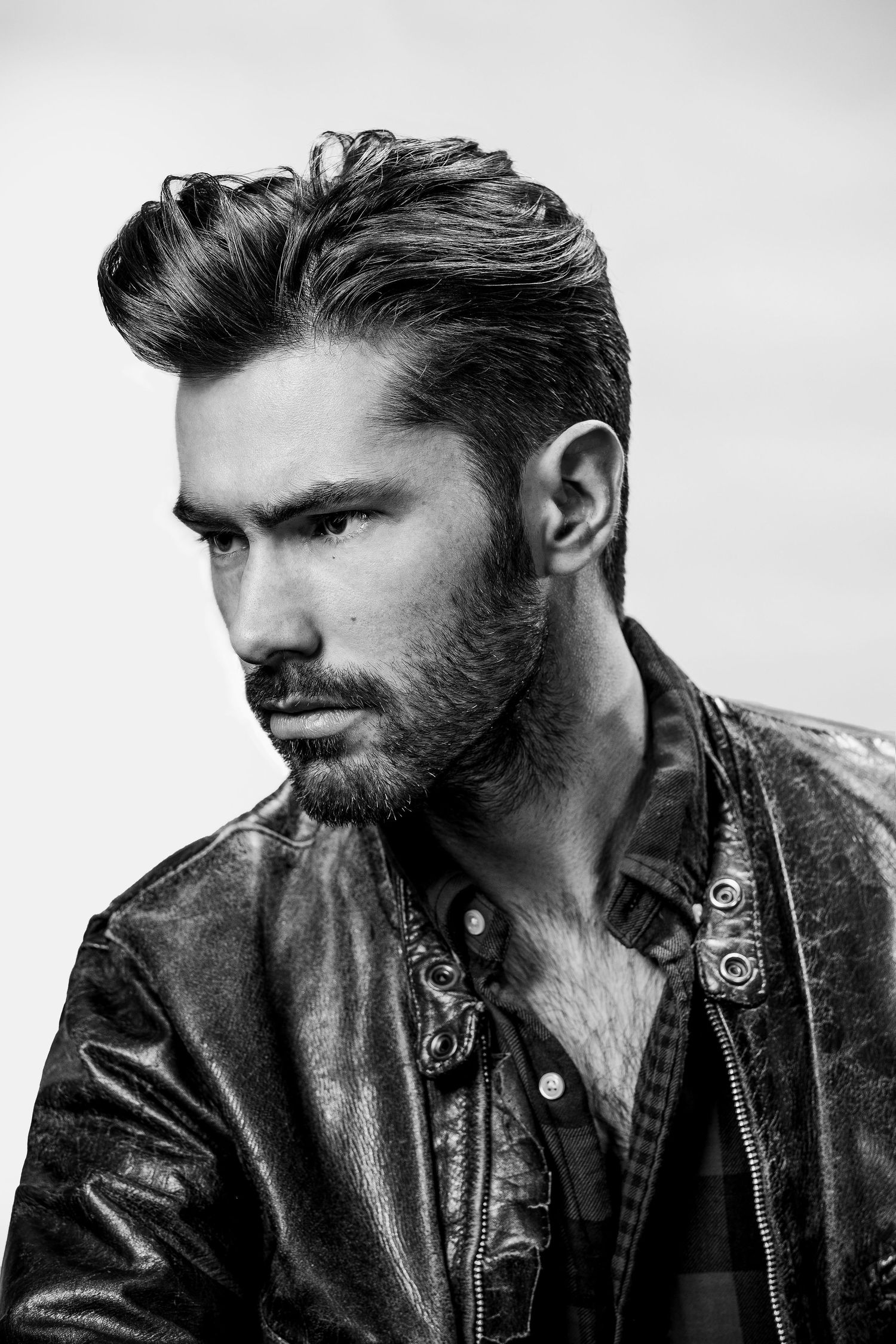 Dramatic black and white portrait of person in leather jacket with styled dark hair.