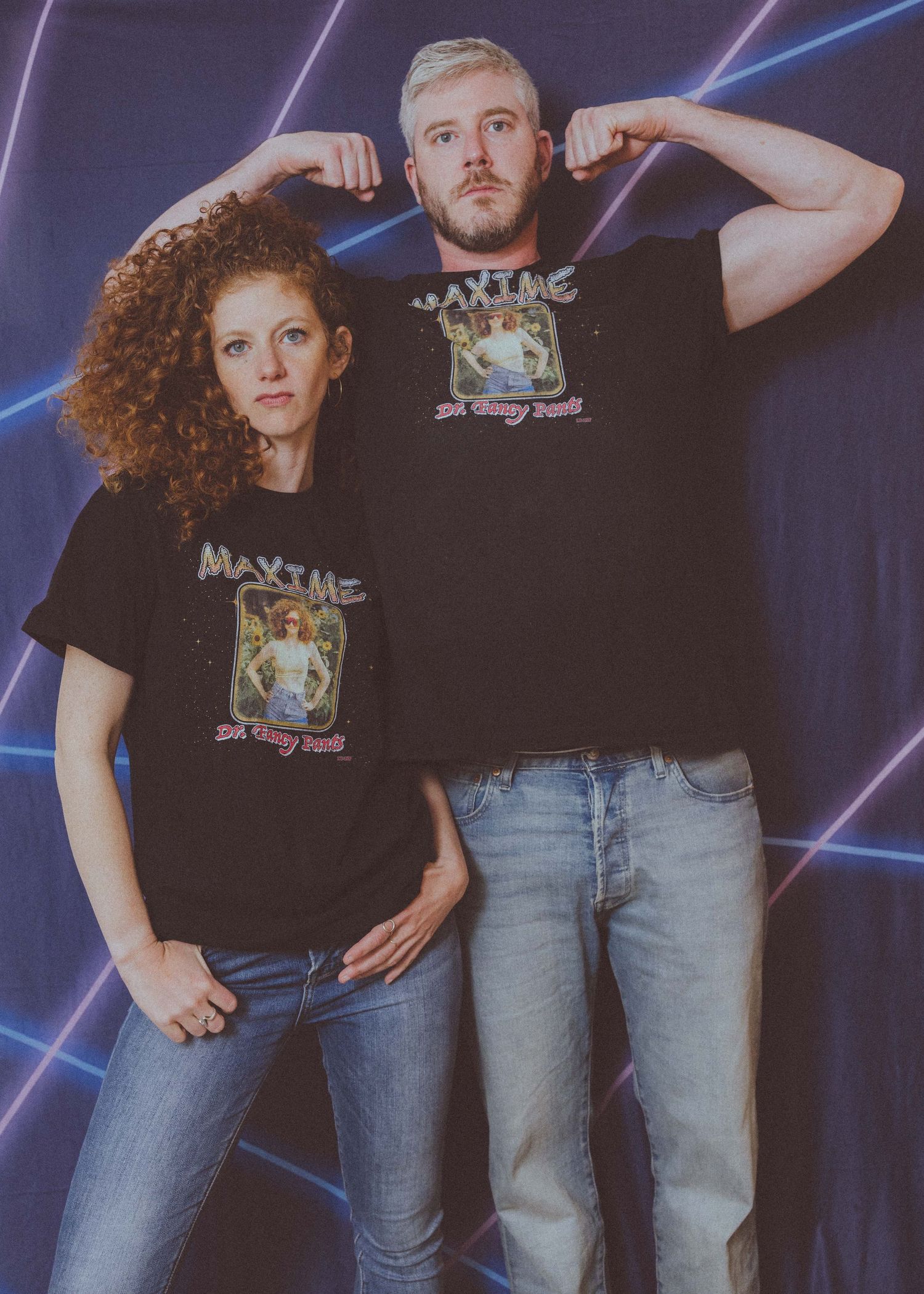 Two people wearing matching graphic t-shirts posing against a neon-lit background.