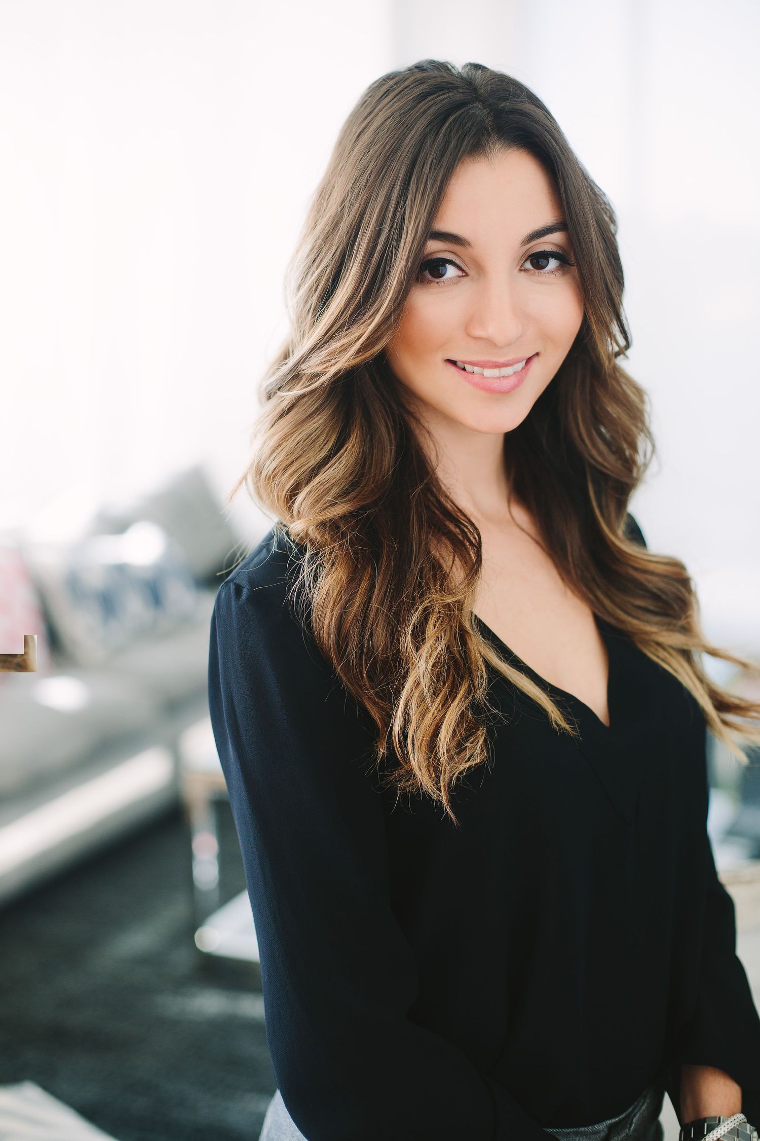 Woman with long wavy ombre hair smiles while wearing black top in studio setting.