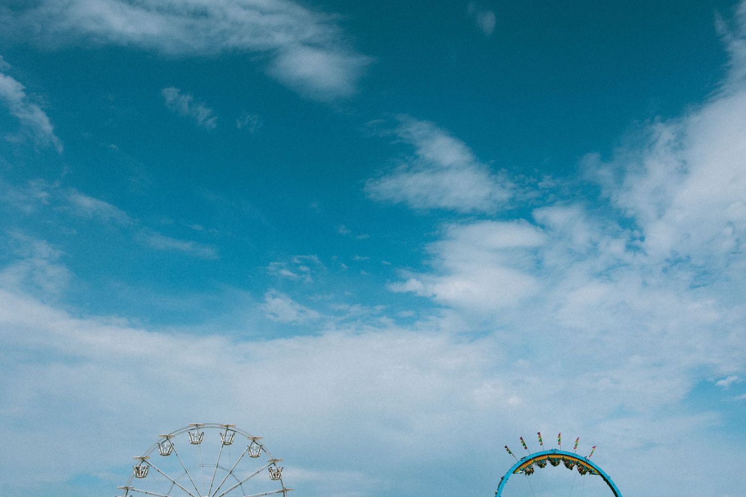 Silhouettes of ferris wheels against a bright blue sky with wispy white clouds.