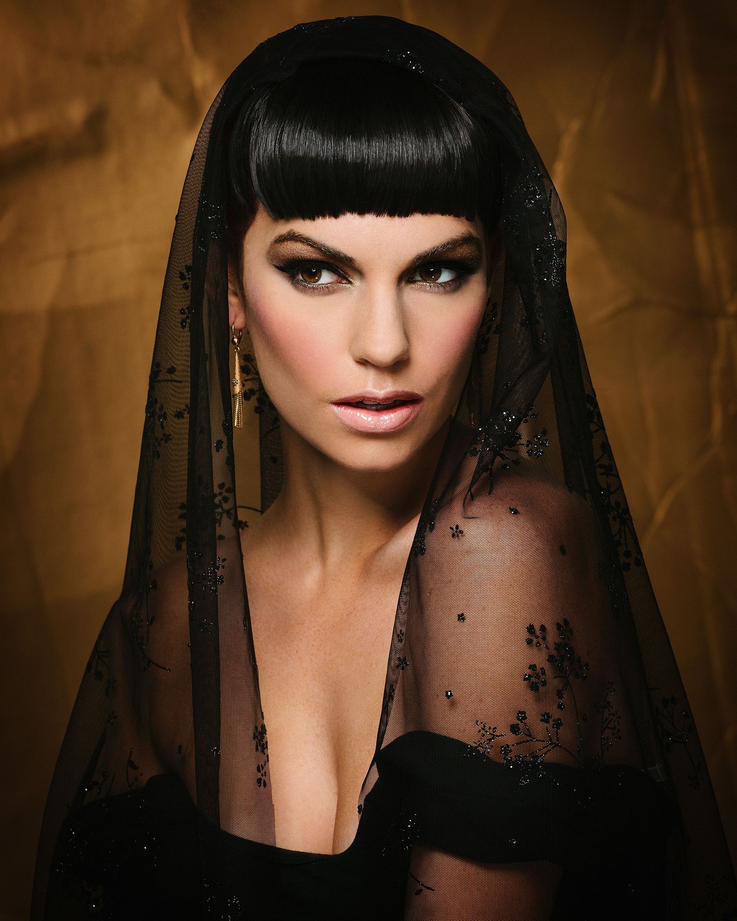 Dramatic portrait of a woman with black bangs wearing a sheer black veil.