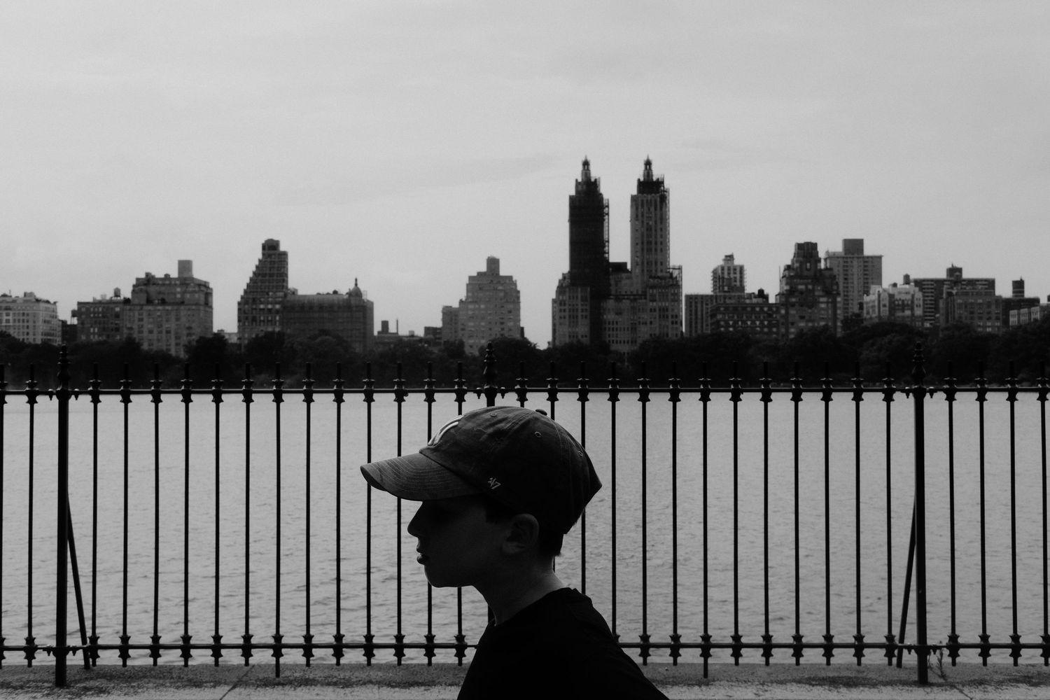 Silhouette of a person against iconic Manhattan skyline through metal railings.