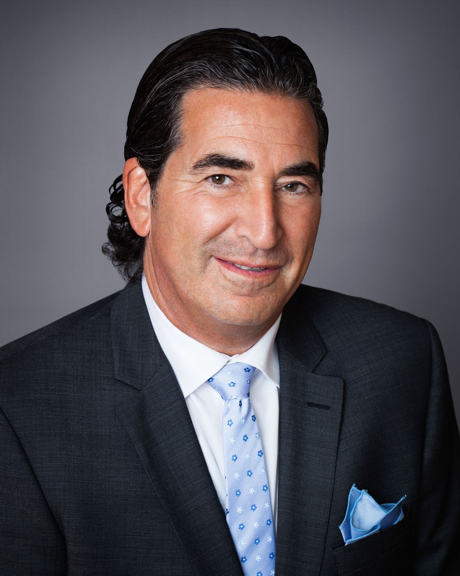 Professional headshot of a businessman in a dark suit and light blue tie.