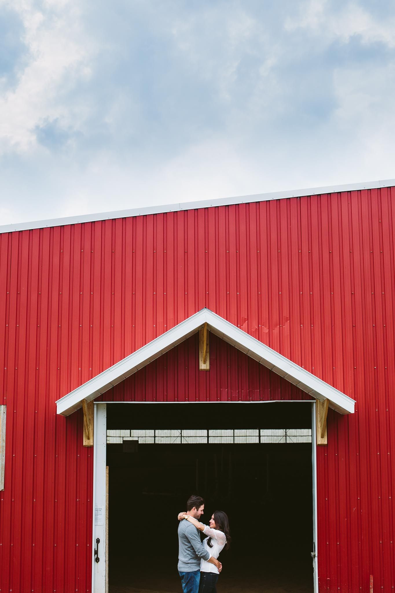 A couple shares an intimate moment in front of a large red barn door.