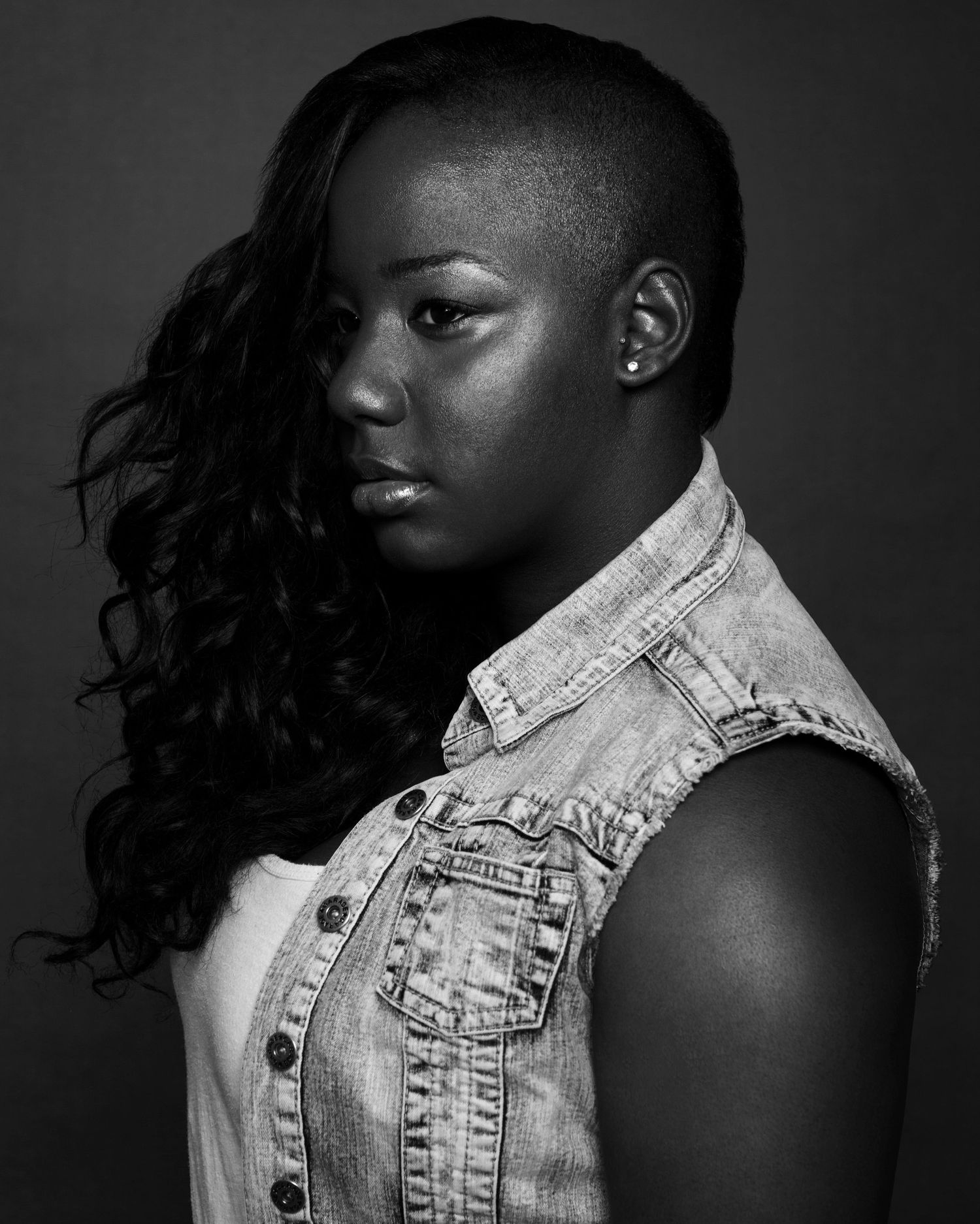 Artistic black and white portrait wearing denim vest with dramatic side lighting.