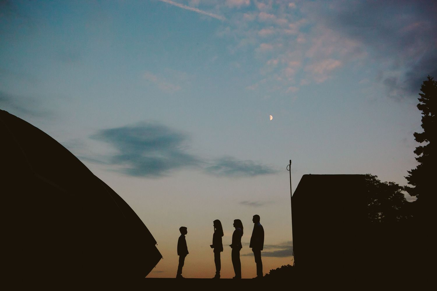 Silhouettes of people standing against sunset sky with moon.