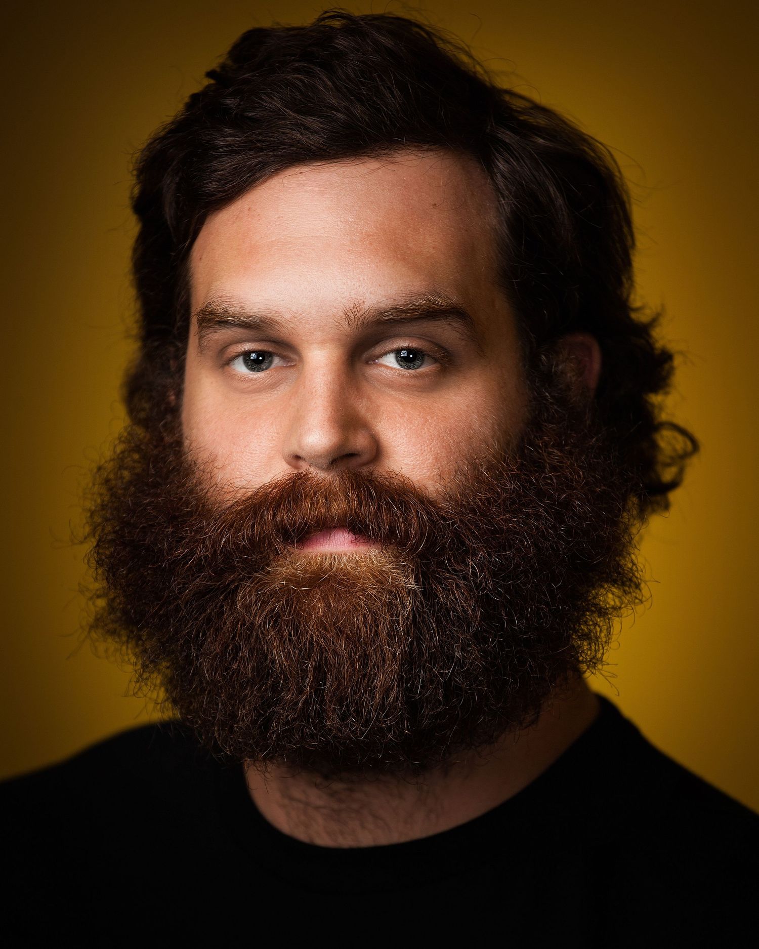 Close-up portrait of a person with a full dark beard against a warm golden background.