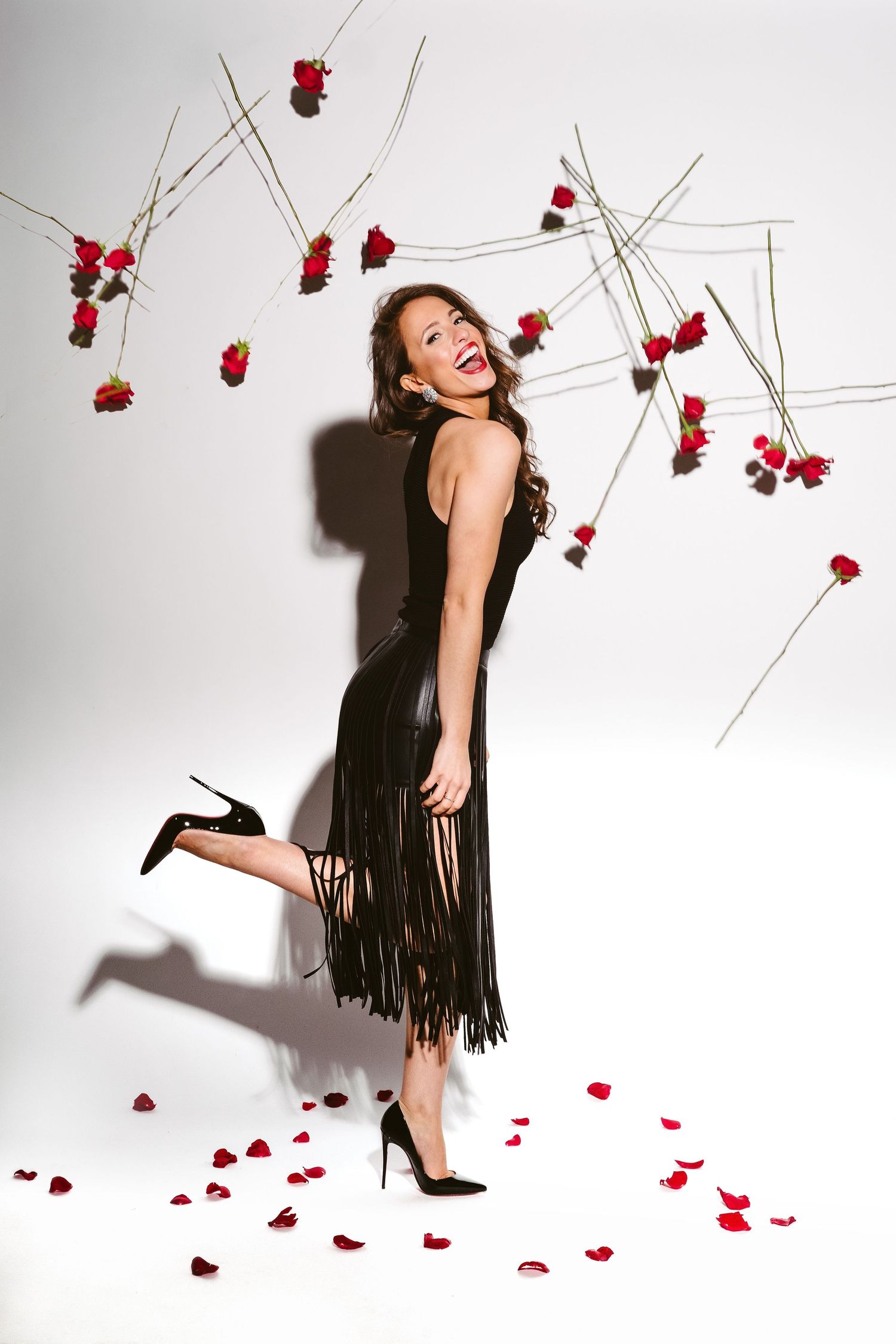 Playful fashion photo with floating red roses and model in black fringe dress.