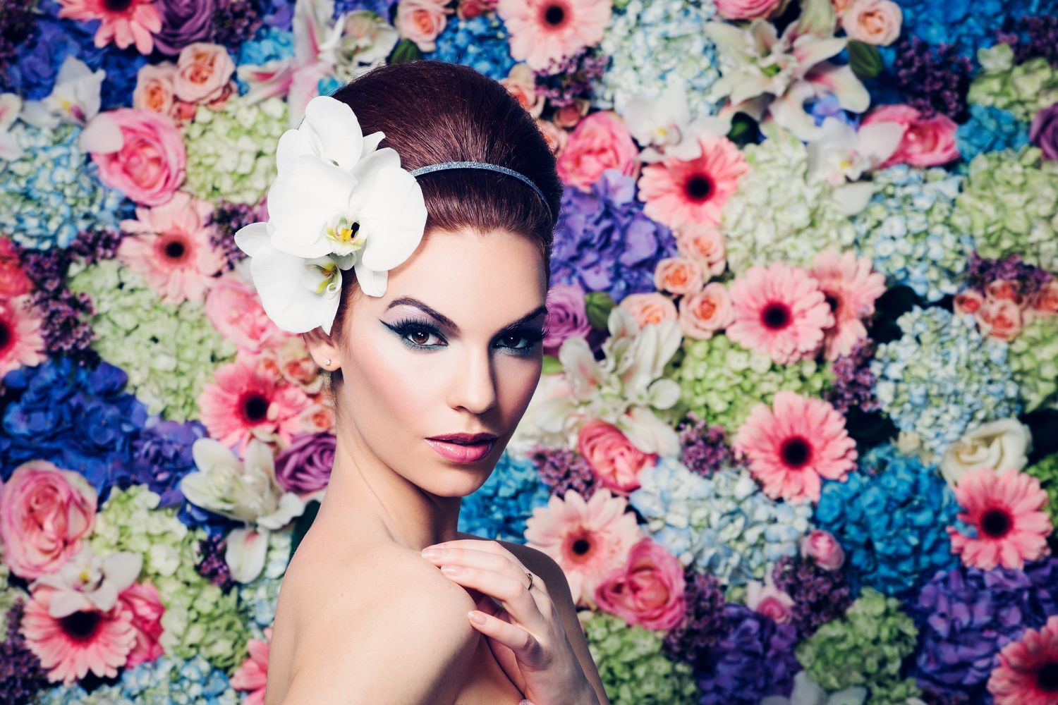Dramatic beauty shot against colorful floral backdrop with pink gerbera daisies and blue hydrangeas.