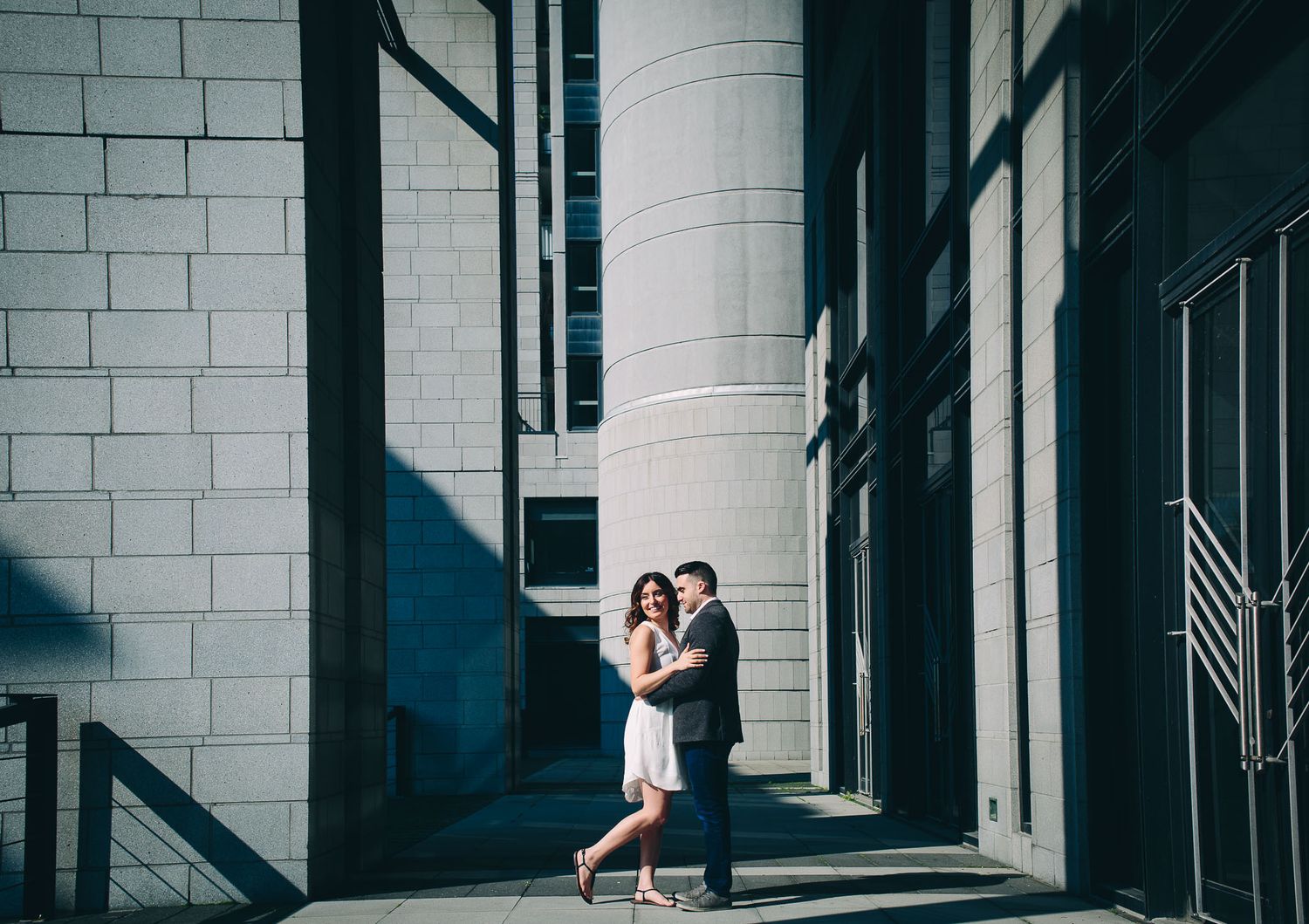 A couple dances together in dramatic lighting against a modern architectural backdrop.