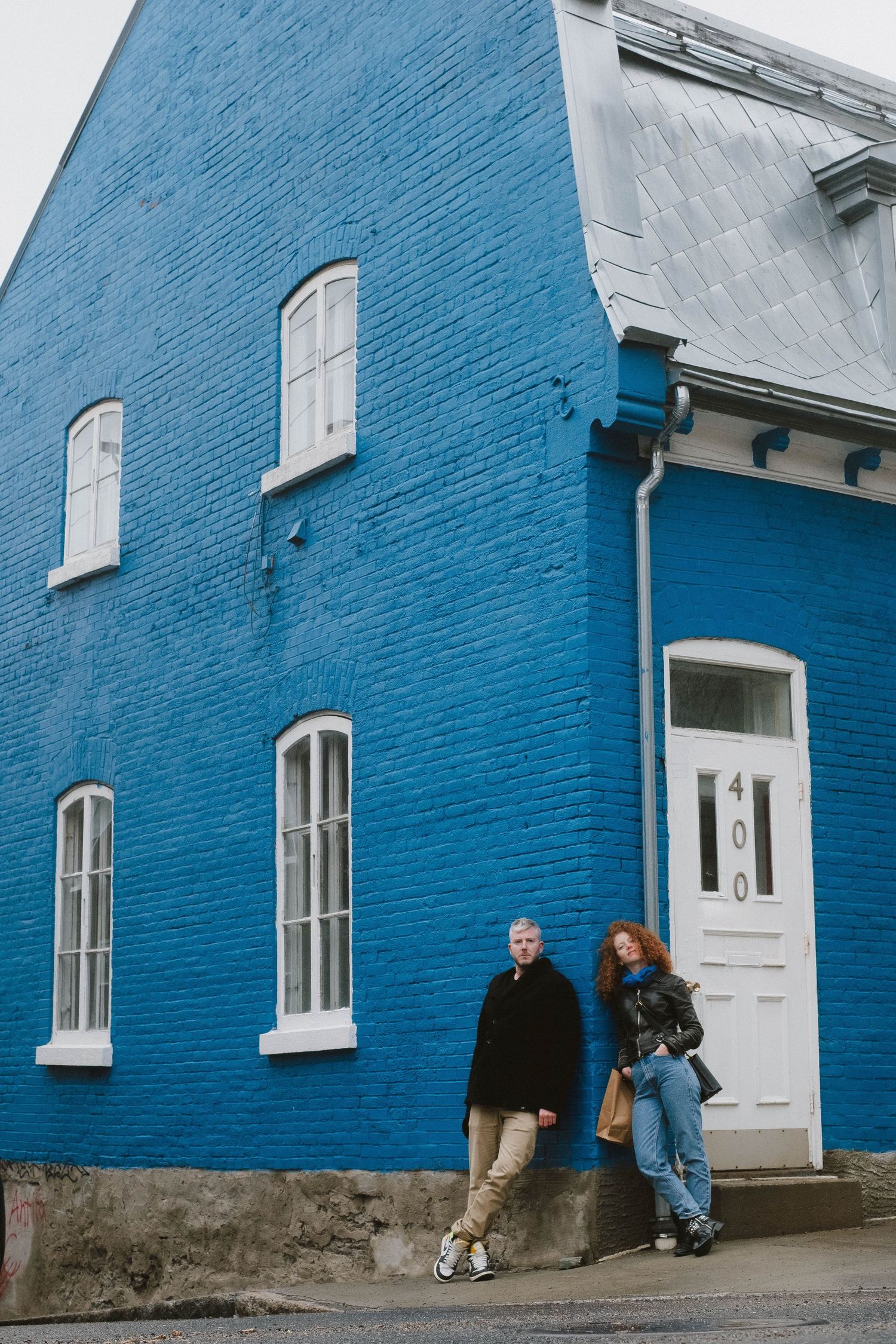 Two people lean against bright blue building exterior with white trim and multiple windows.