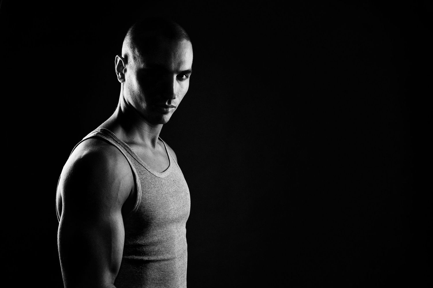 Dramatic side profile of an athletic man in tank top against dark background.