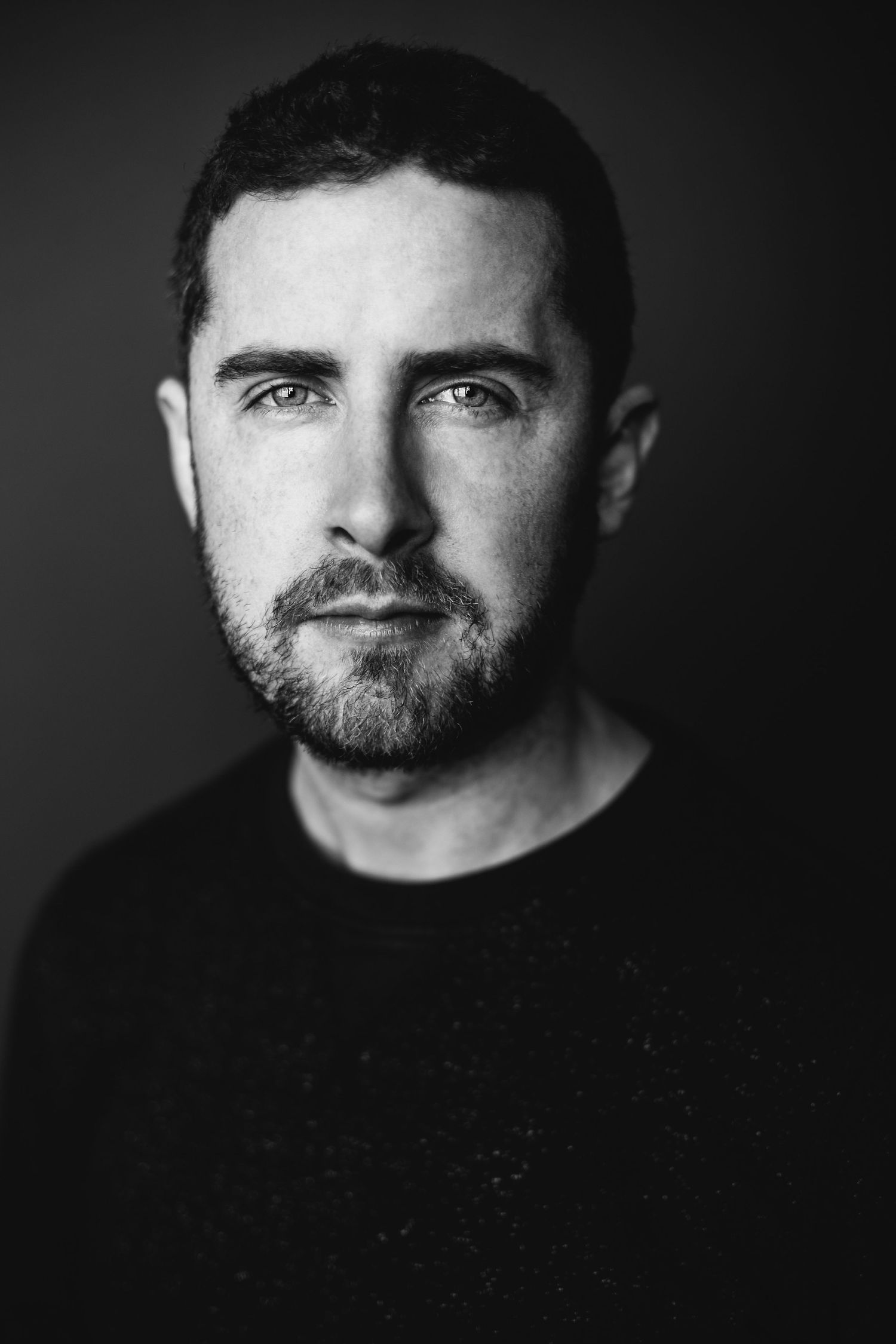 Black and white portrait of bearded man against dark background.