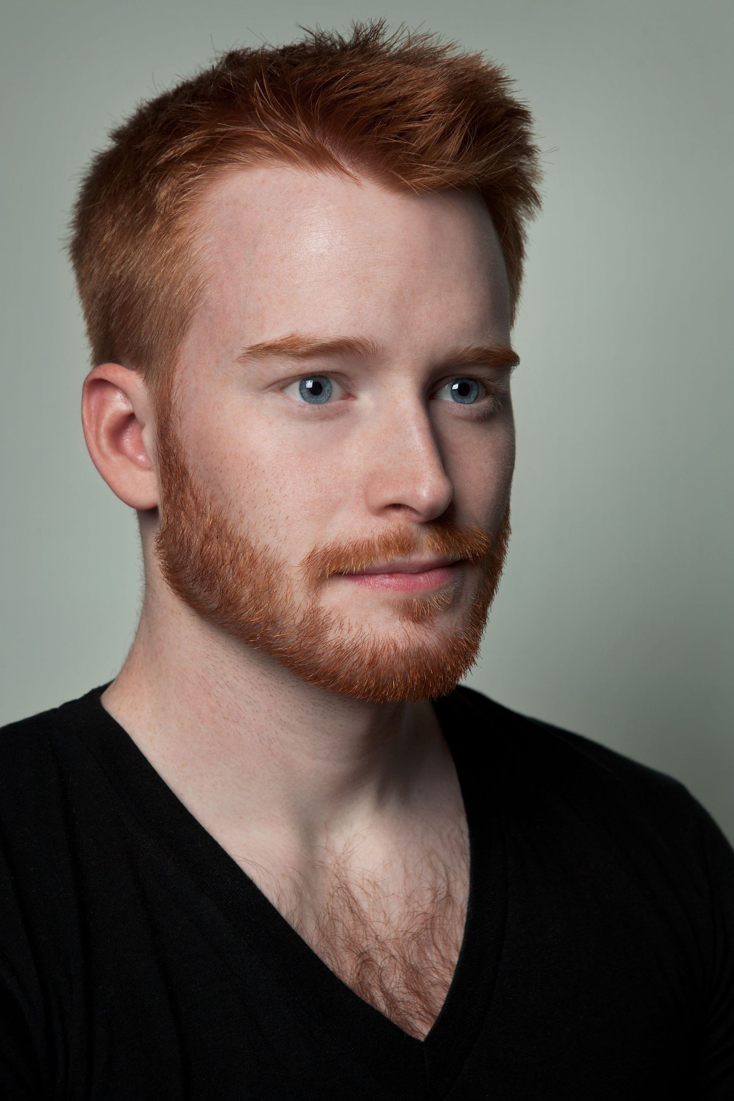 Close-up portrait of a man with red hair and beard in a black v-neck shirt.