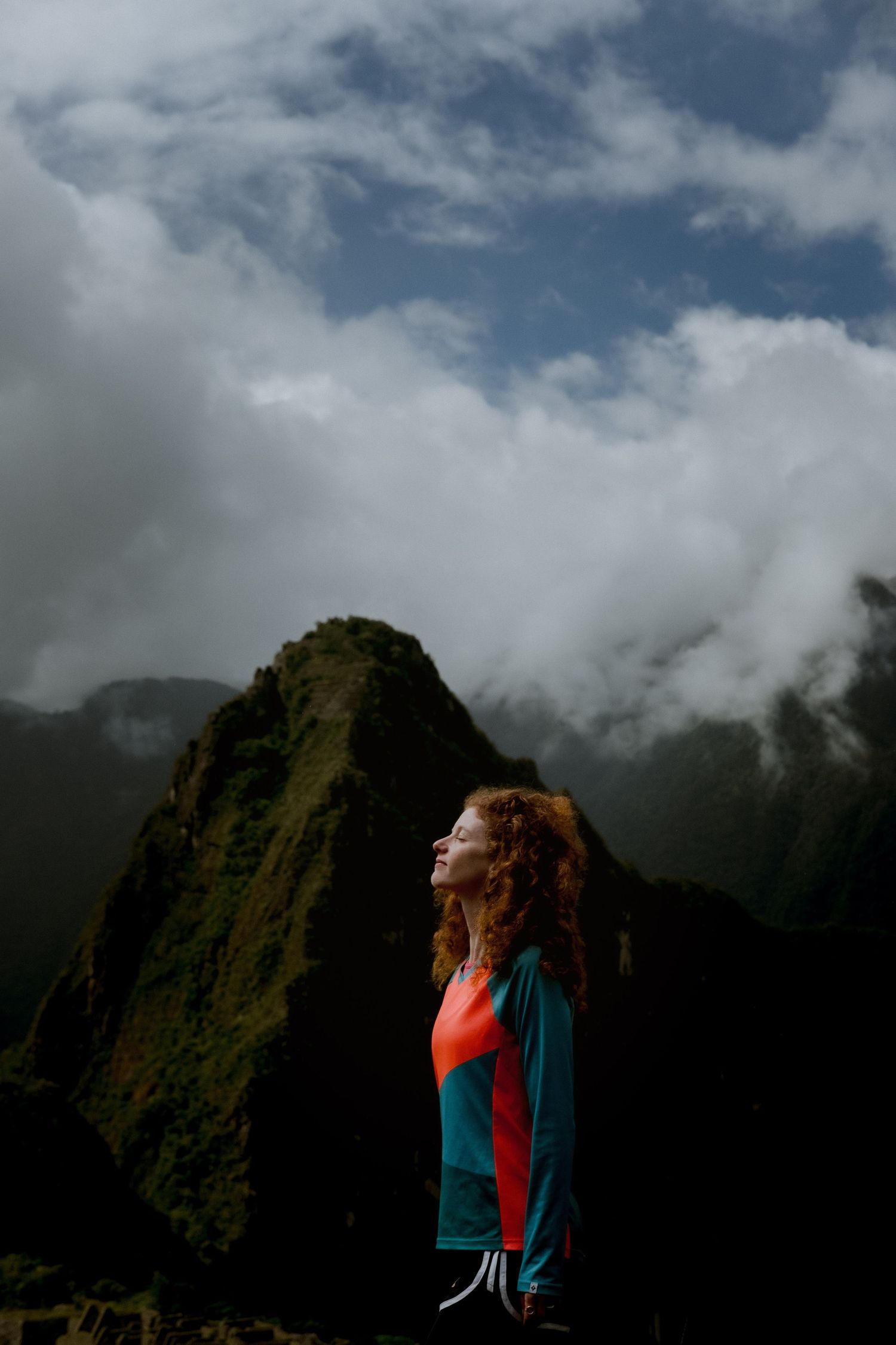 Person in colorful jacket enjoying mountain views against dramatic cloudy backdrop.