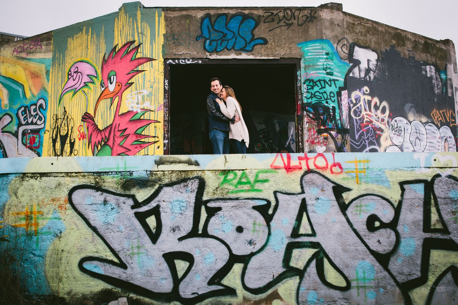 Urban couple embraces in front of colorful graffiti wall in abandoned building.
