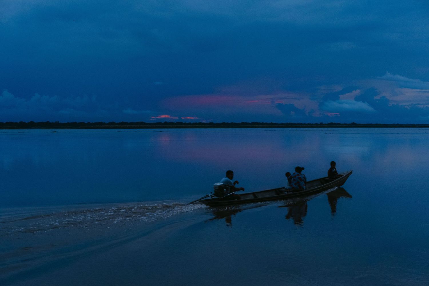 Silhouetted boat with passengers glides across calm blue waters during a vivid twilight.