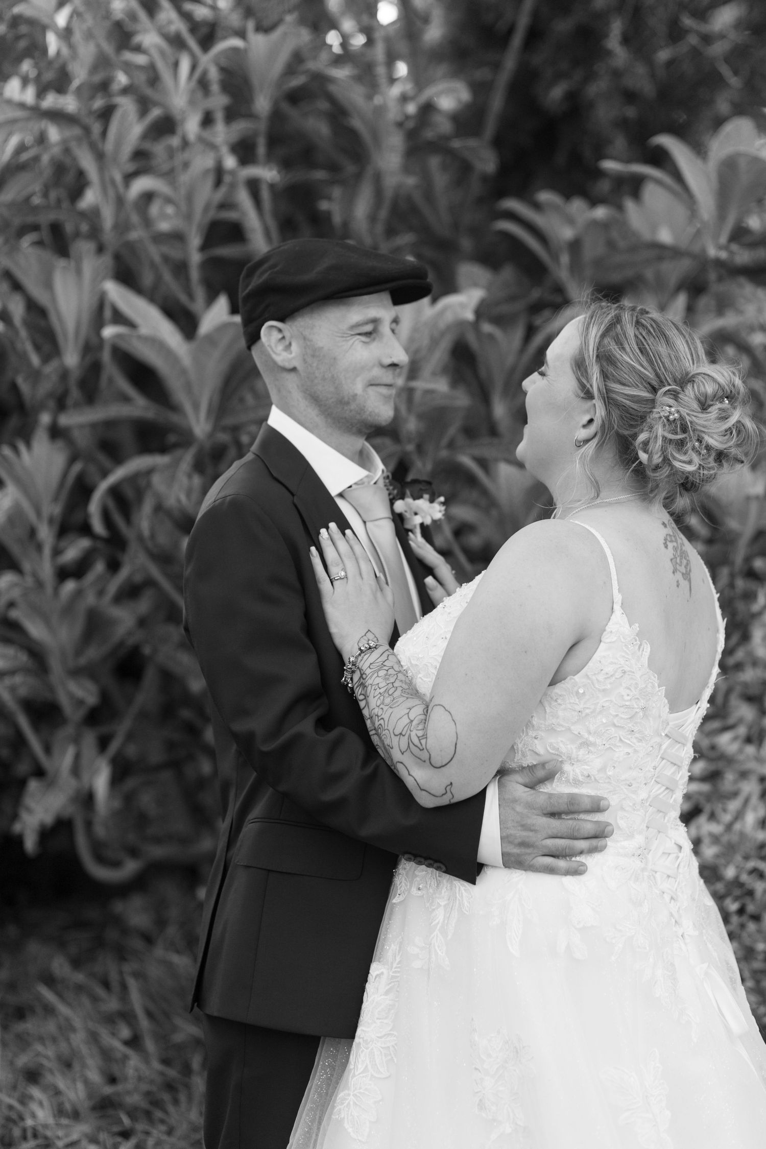 Black and White photo of a bride and groom stood chest to chest. The groom’s hands around his bride’s waist, her hands resting on his lapels