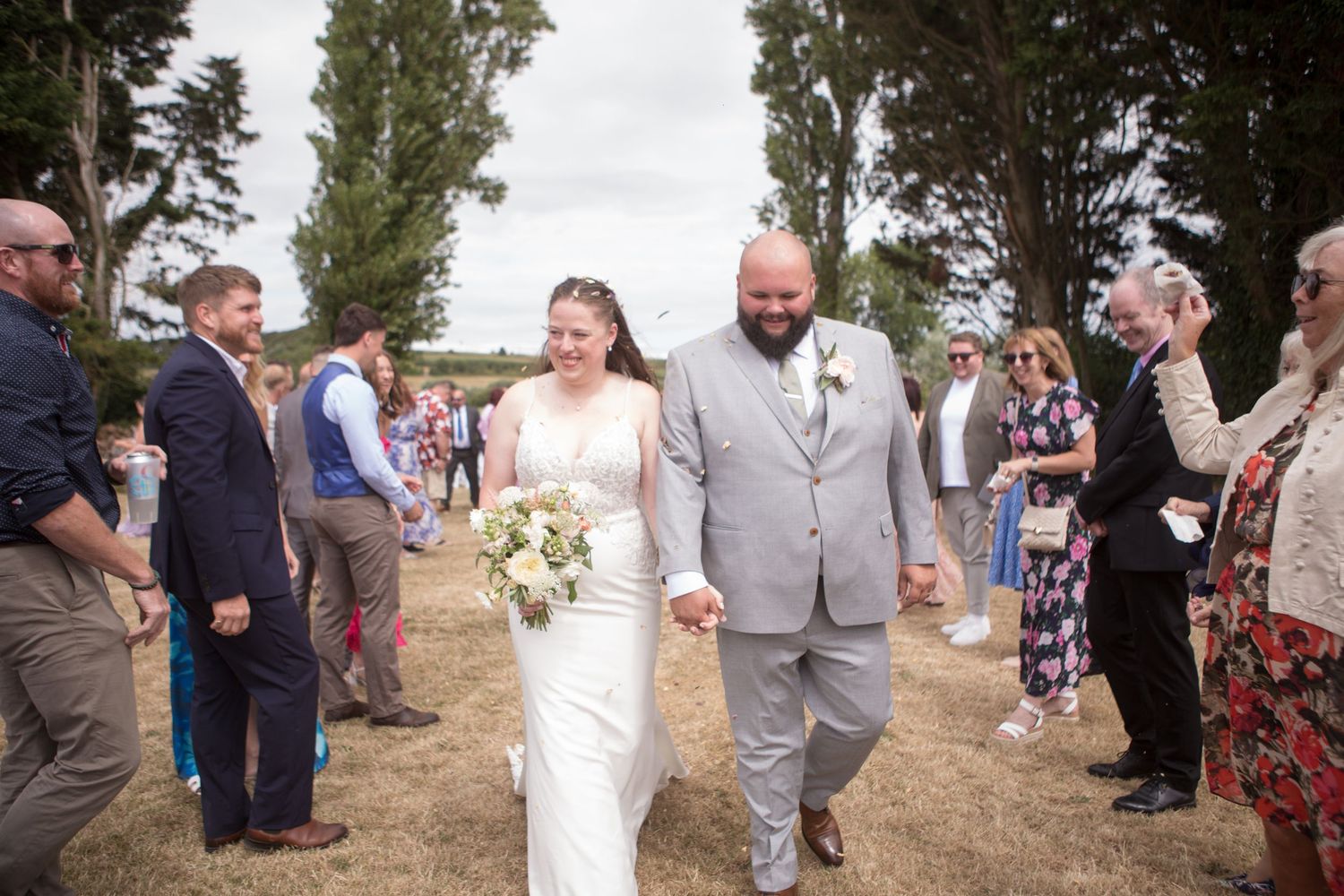 Bride and Groom walk together through a tunnel of their family members at the end of their confetti throw