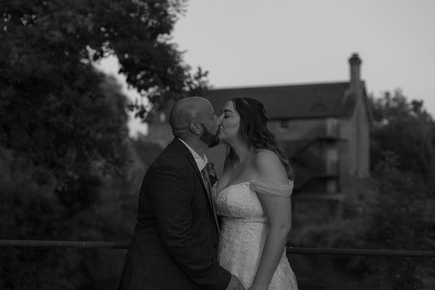 Bride and Groom share a kiss on a bridge, with Sopley Mill in the distance behind them.