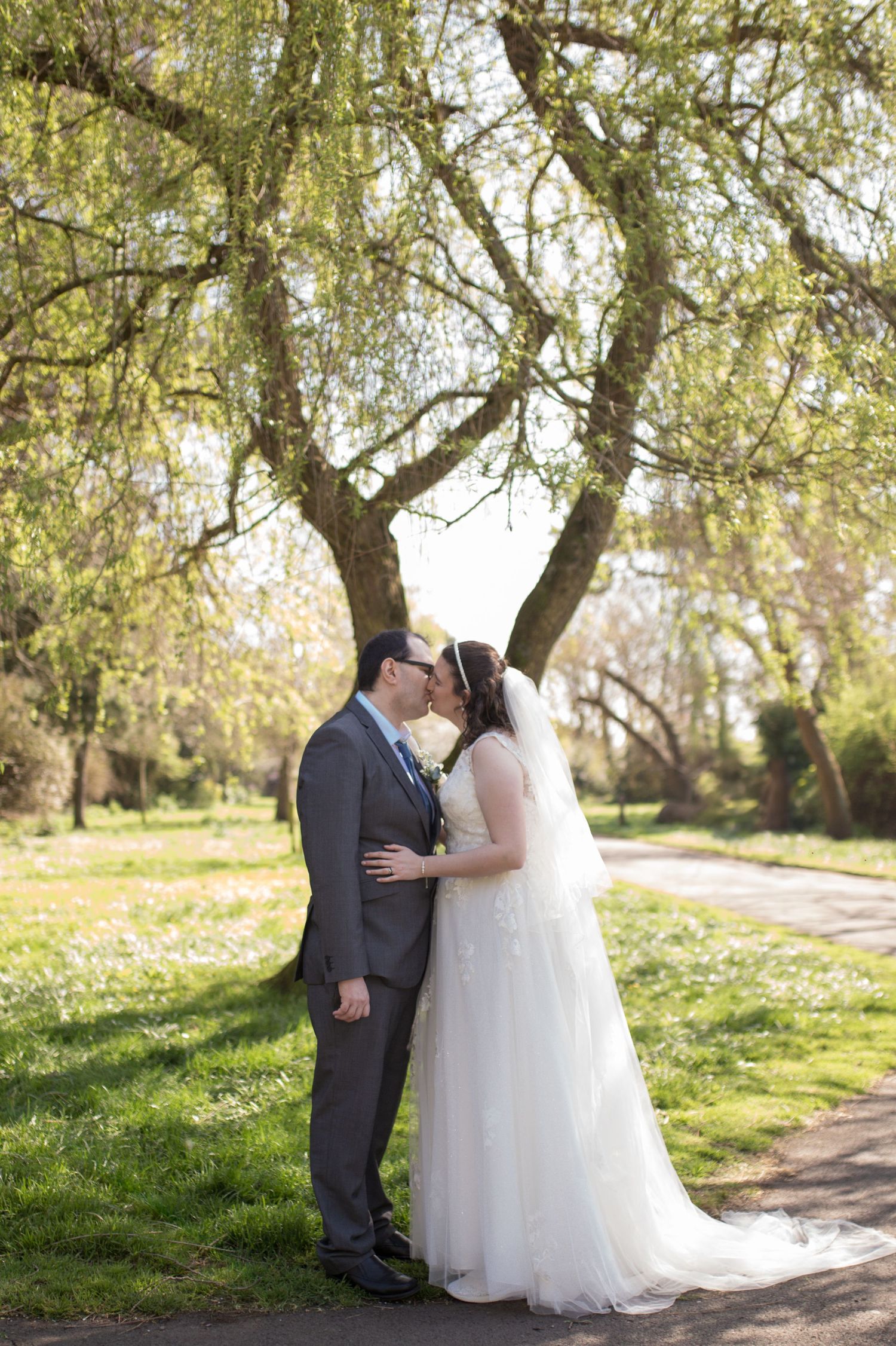 Bride and Groom share a kiss under a beautiful green tree, in the middle of Radipole Park in the middle of spring.
