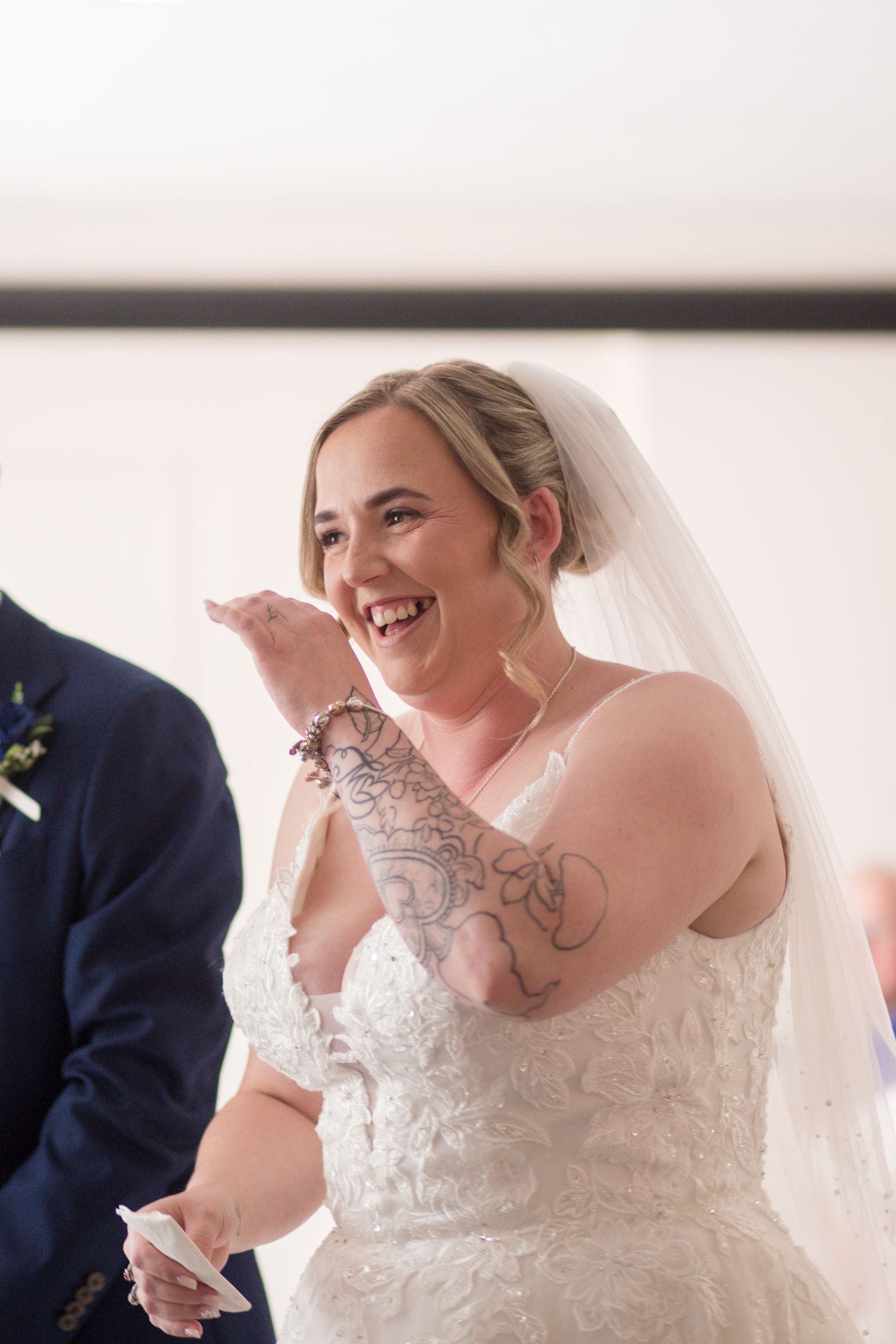 Bride brings her hand up to her face to hide her laugh in the middle of her wedding ceremony.