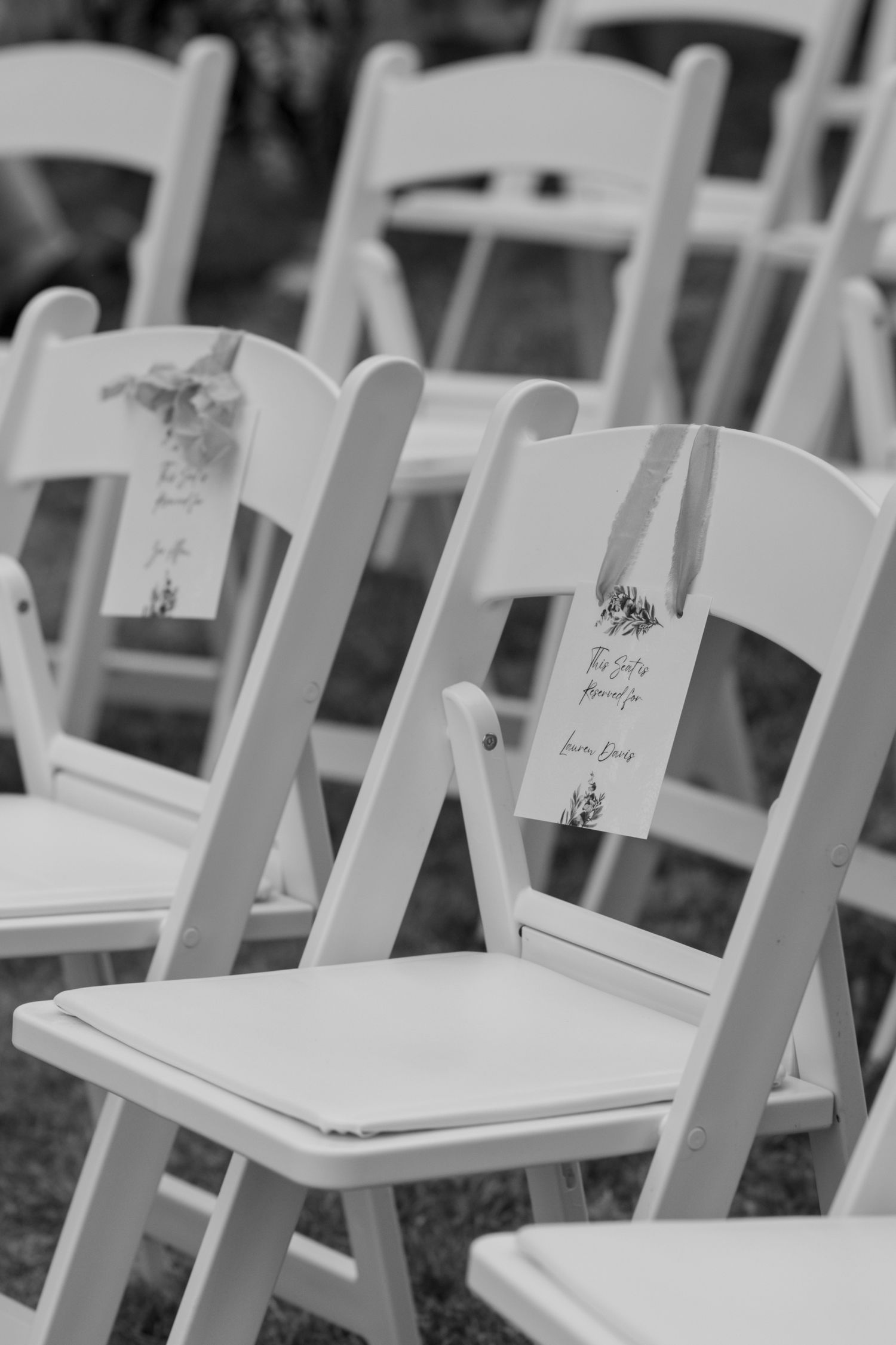 Black and white photo of ceremony chairs, with hanging reserved signs for the bridesmaids.