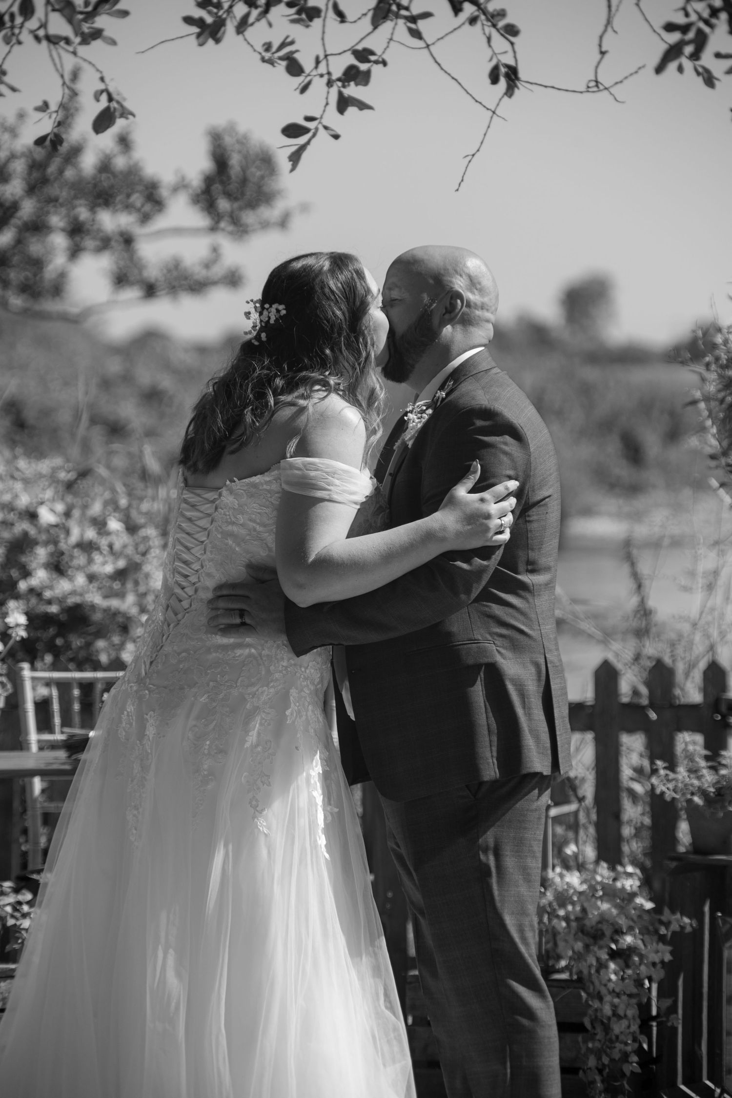 Black and white photo of a bride and groom sharing their first kiss in their outdoor ceremony