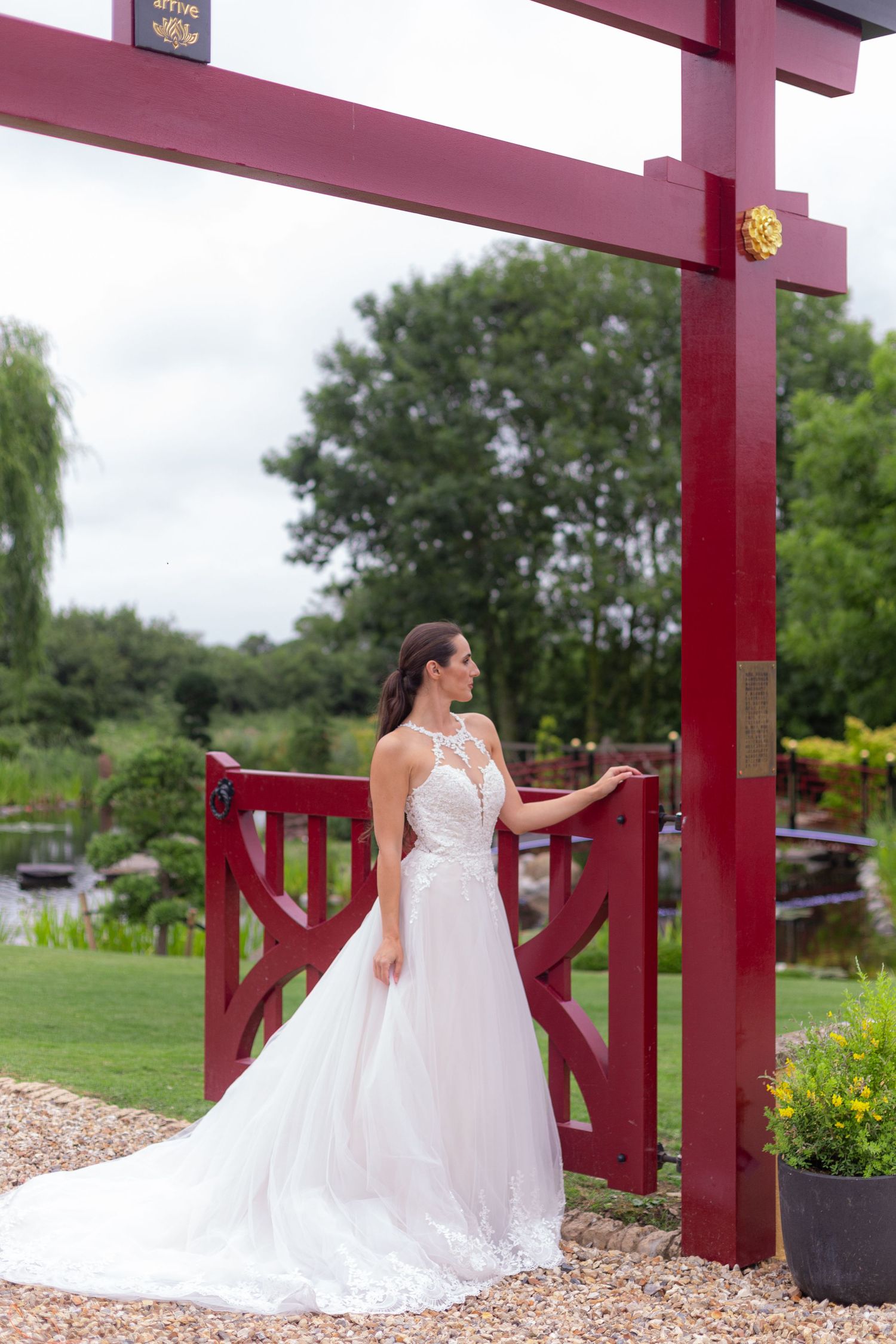 A bride poses for a photo in an elegant ballgown next to the red posts of a Japanese themed gate.