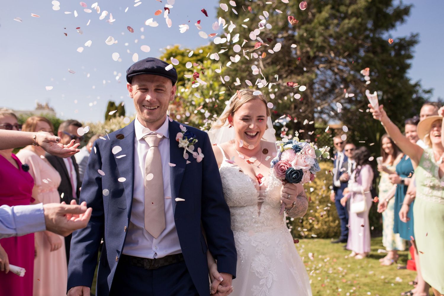 Bride and Groom laugh as they walk between their guest, being showered by confetti